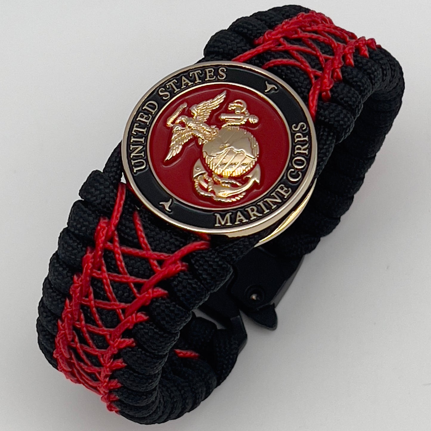 Thick, wide, rigid and comfortable braided United States Marine Corps bracelet featuring a 24K gold plated USMC Eagle Globe and Anchor medallion, a black Cobra style tactical buckle and woven with black 550 paracord and Imperial Red nano and micro cord.