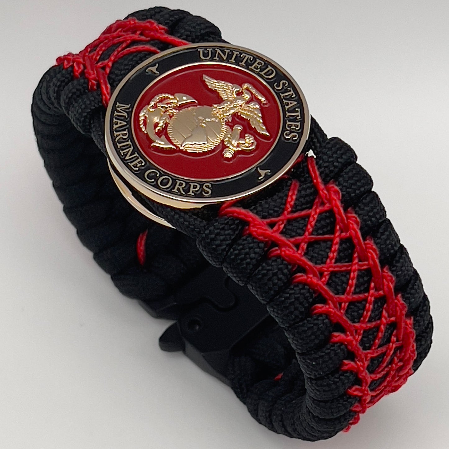 Thick, wide, rigid and comfortable braided United States Marine Corps bracelet featuring a 24K gold plated USMC Eagle Globe and Anchor medallion, a black Cobra style tactical buckle and woven with black 550 paracord and Imperial Red nano and micro cord.