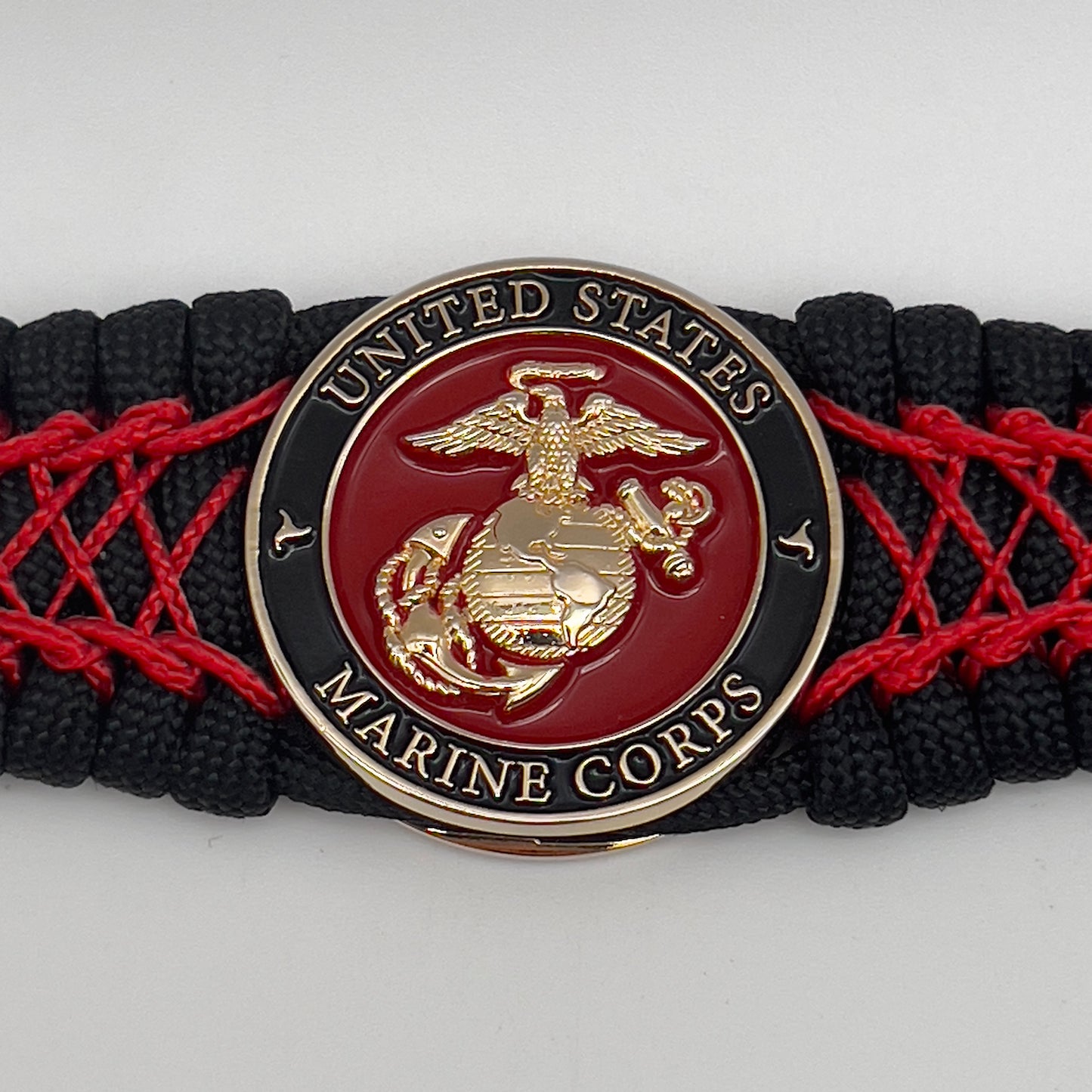 Thick, wide, rigid and comfortable braided United States Marine Corps bracelet featuring a 24K gold plated USMC Eagle Globe and Anchor medallion, a black Cobra style tactical buckle and woven with black 550 paracord and Imperial Red nano and micro cord.