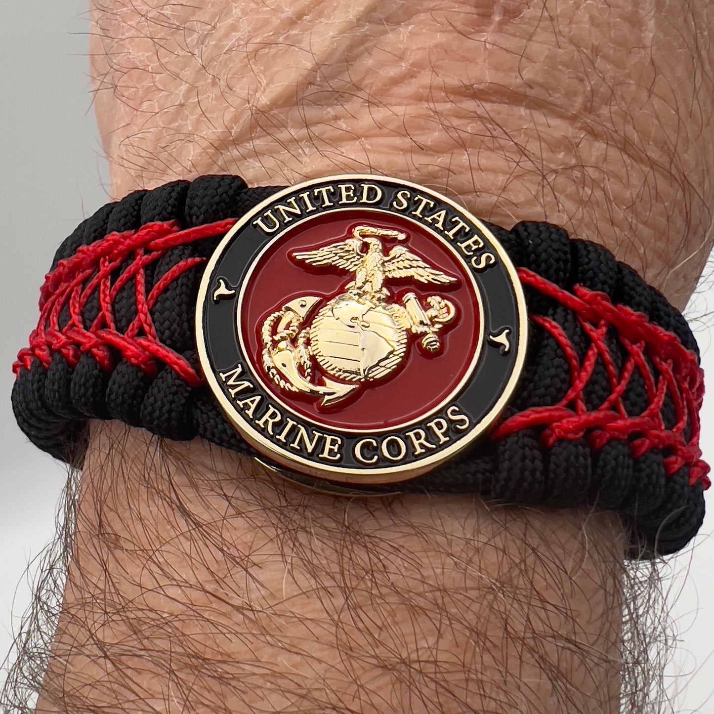 Thick, wide, rigid and comfortable braided United States Marine Corps bracelet featuring a 24K gold plated USMC Eagle Globe and Anchor medallion, a black Cobra style tactical buckle and woven with black 550 paracord and Imperial Red nano and micro cord.