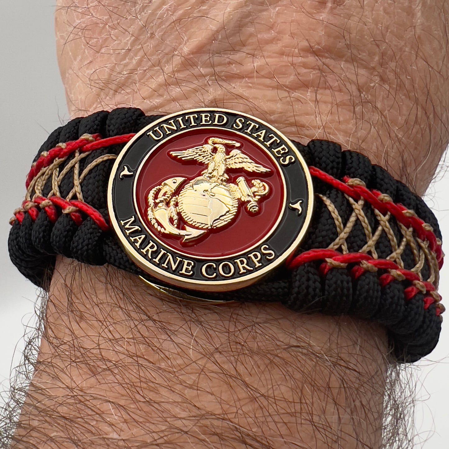 Thick, wide, rigid and comfortable braided United States Marine Corps bracelet featuring a 24K gold plated USMC Eagle Globe and Anchor medallion, a black Cobra style tactical buckle and woven with black 550 paracord and Imperial Red micro and gold nano cord.