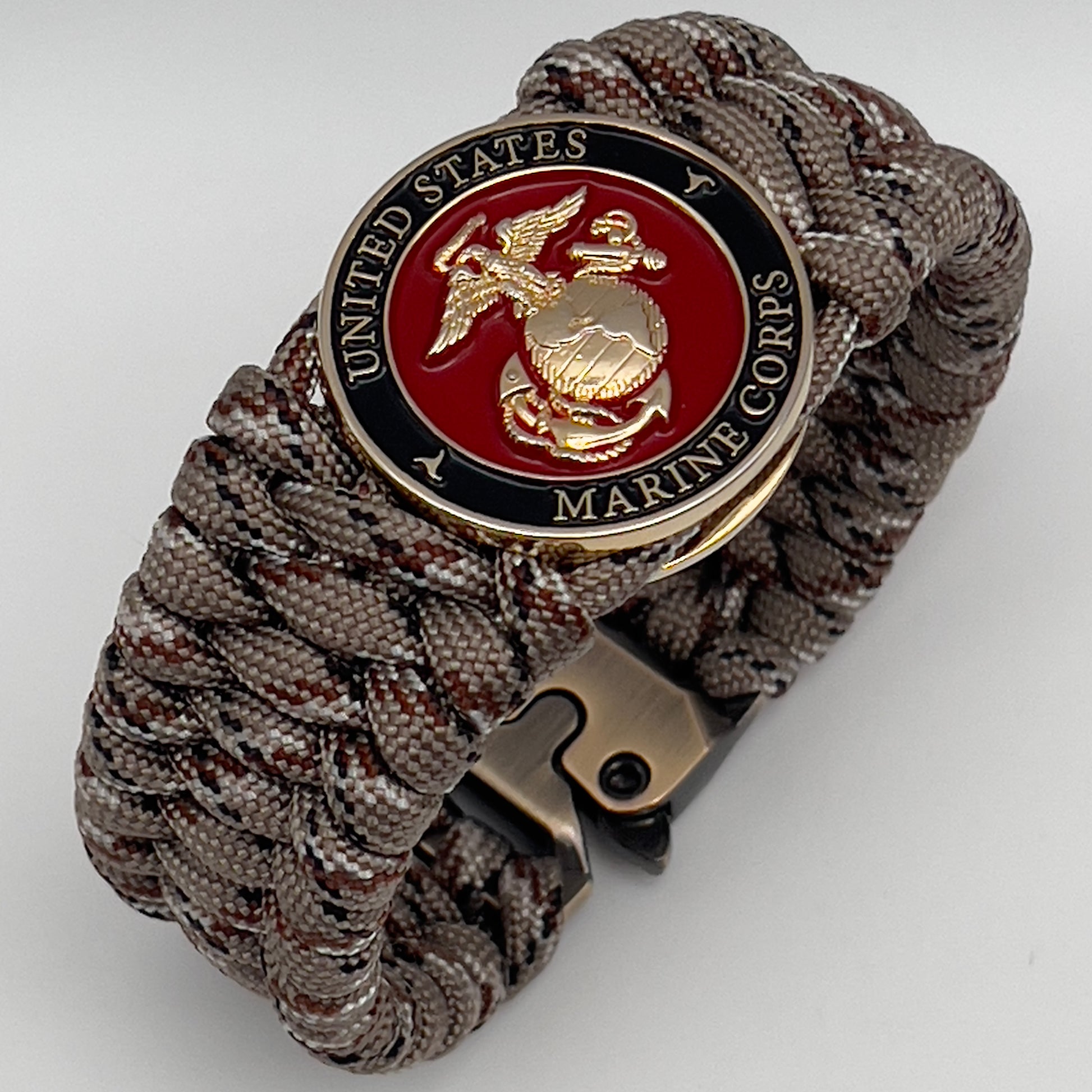 Thick, wide, semi-rigid and comfortable braided United States Marine Corps bracelet featuring a 24K gold plated USMC Eagle Globe and Anchor medallion, a gold Cobra style tactical buckle and woven with Desert Camo 550 paracord.