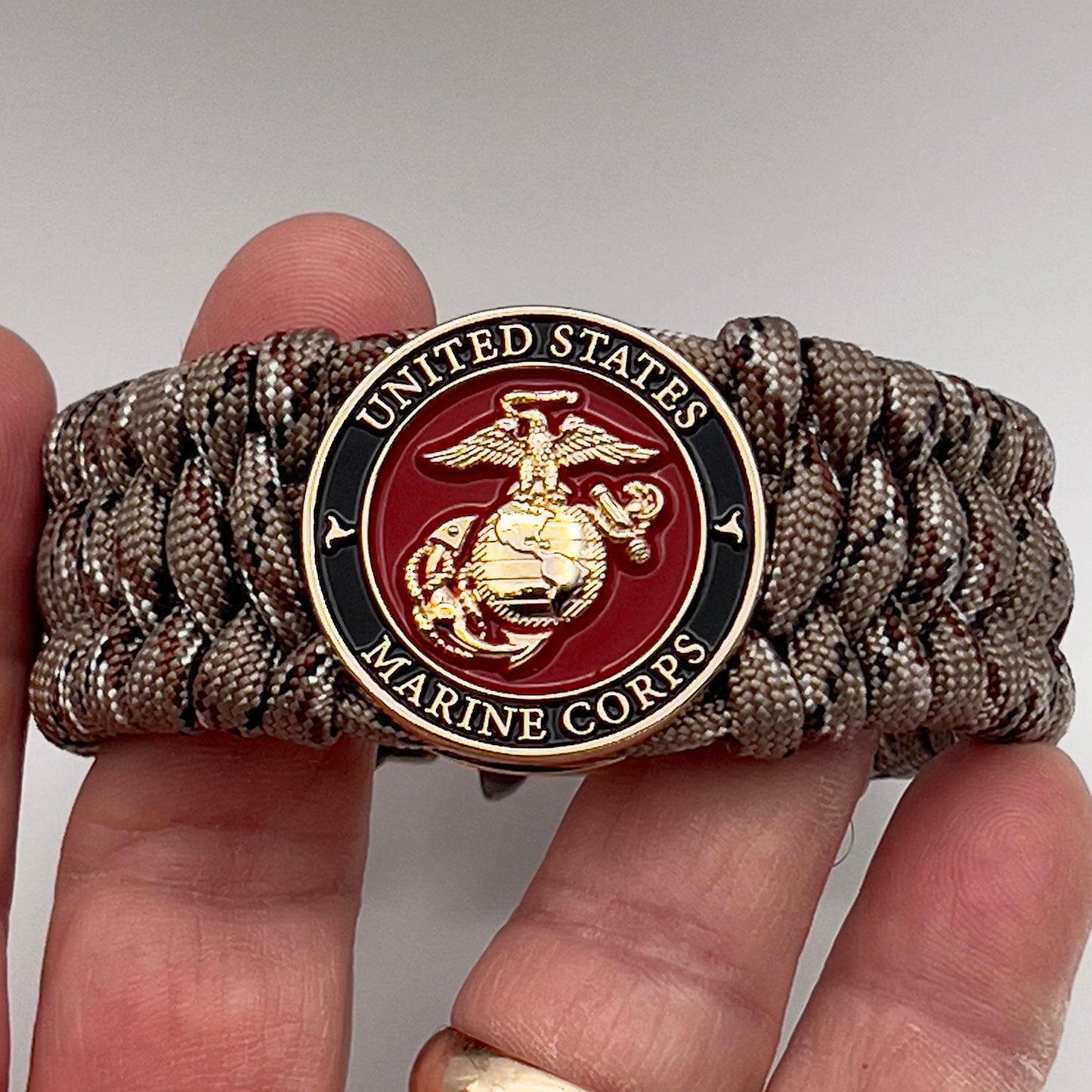 Thick, wide, semi-rigid and comfortable braided United States Marine Corps bracelet featuring a 24K gold plated USMC Eagle Globe and Anchor medallion, a gold Cobra style tactical buckle and woven with Desert Camo 550 paracord.