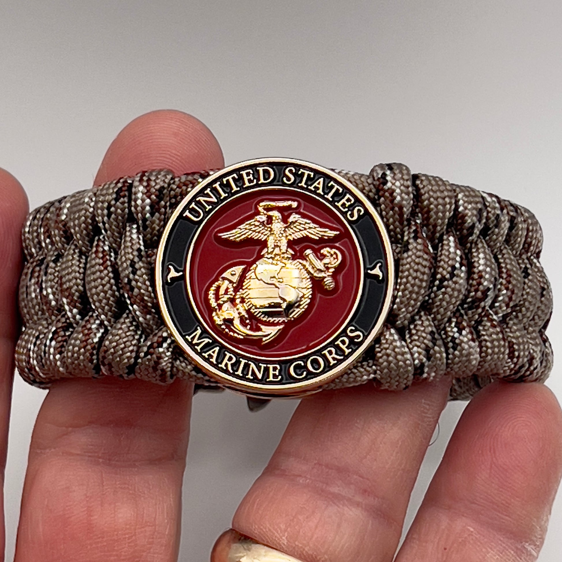 Thick, wide, semi-rigid and comfortable braided United States Marine Corps bracelet featuring a 24K gold plated USMC Eagle Globe and Anchor medallion, a gold Cobra style tactical buckle and woven with Desert Camo 550 paracord.