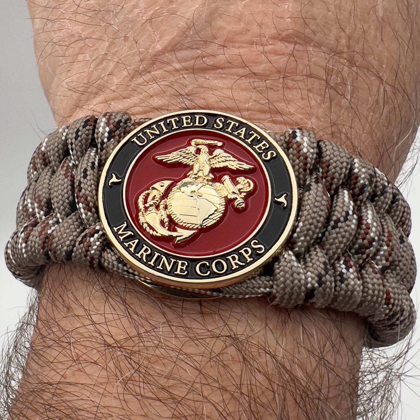 Thick, wide, semi-rigid and comfortable braided United States Marine Corps bracelet featuring a 24K gold plated USMC Eagle Globe and Anchor medallion, a gold Cobra style tactical buckle and woven with Desert Camo 550 paracord.