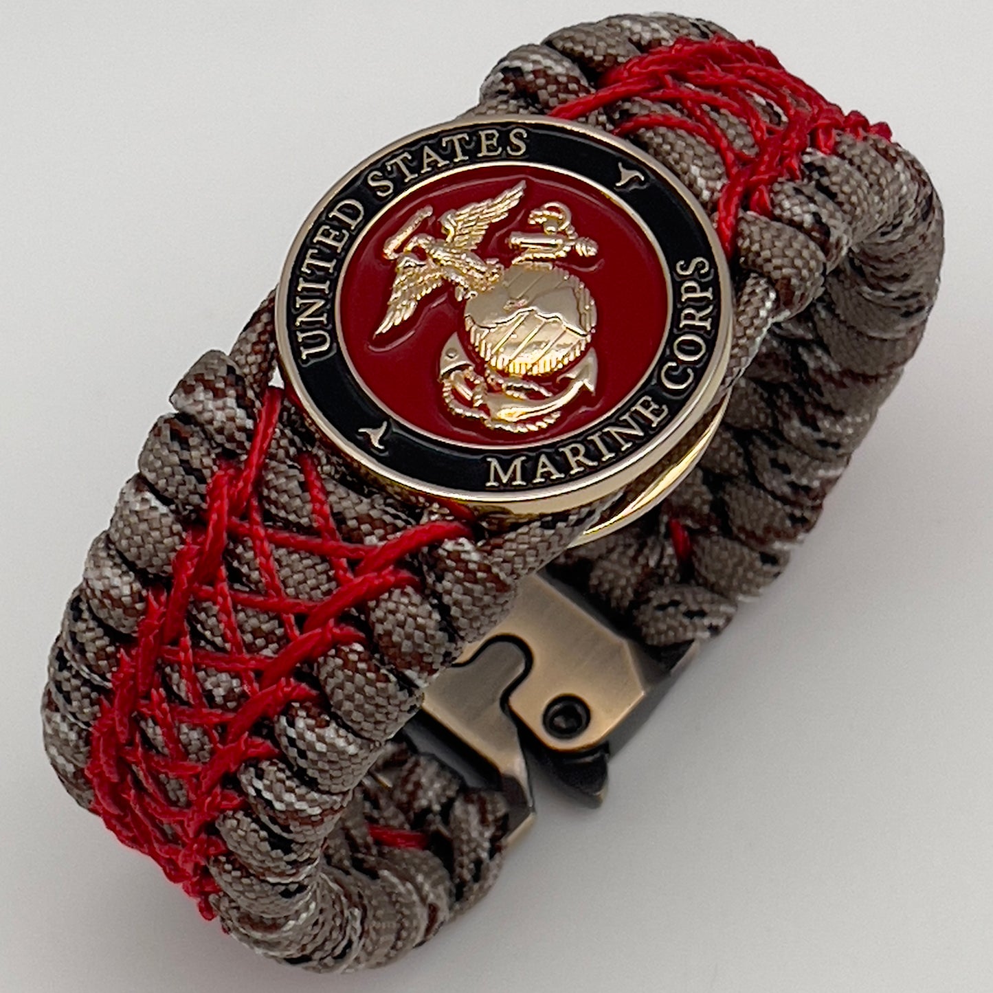 Thick, wide, rigid and comfortable braided United States Marine Corps bracelet featuring a 24K gold plated USMC Eagle Globe and Anchor medallion, a gold Cobra style tactical buckle and woven with Desert Camo 550 paracord and Imperial Red nano and micro cord.