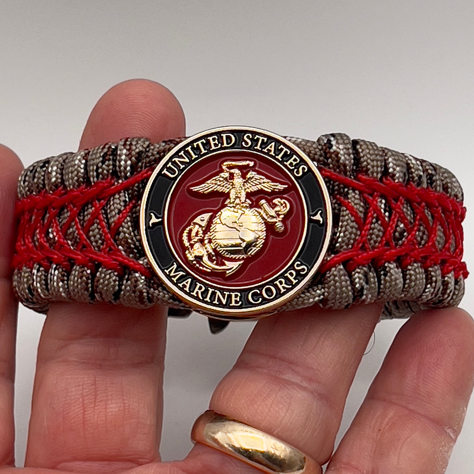 Thick, wide, rigid and comfortable braided United States Marine Corps bracelet featuring a 24K gold plated USMC Eagle Globe and Anchor medallion, a gold Cobra style tactical buckle and woven with Desert Camo 550 paracord and Imperial Red nano and micro cord.