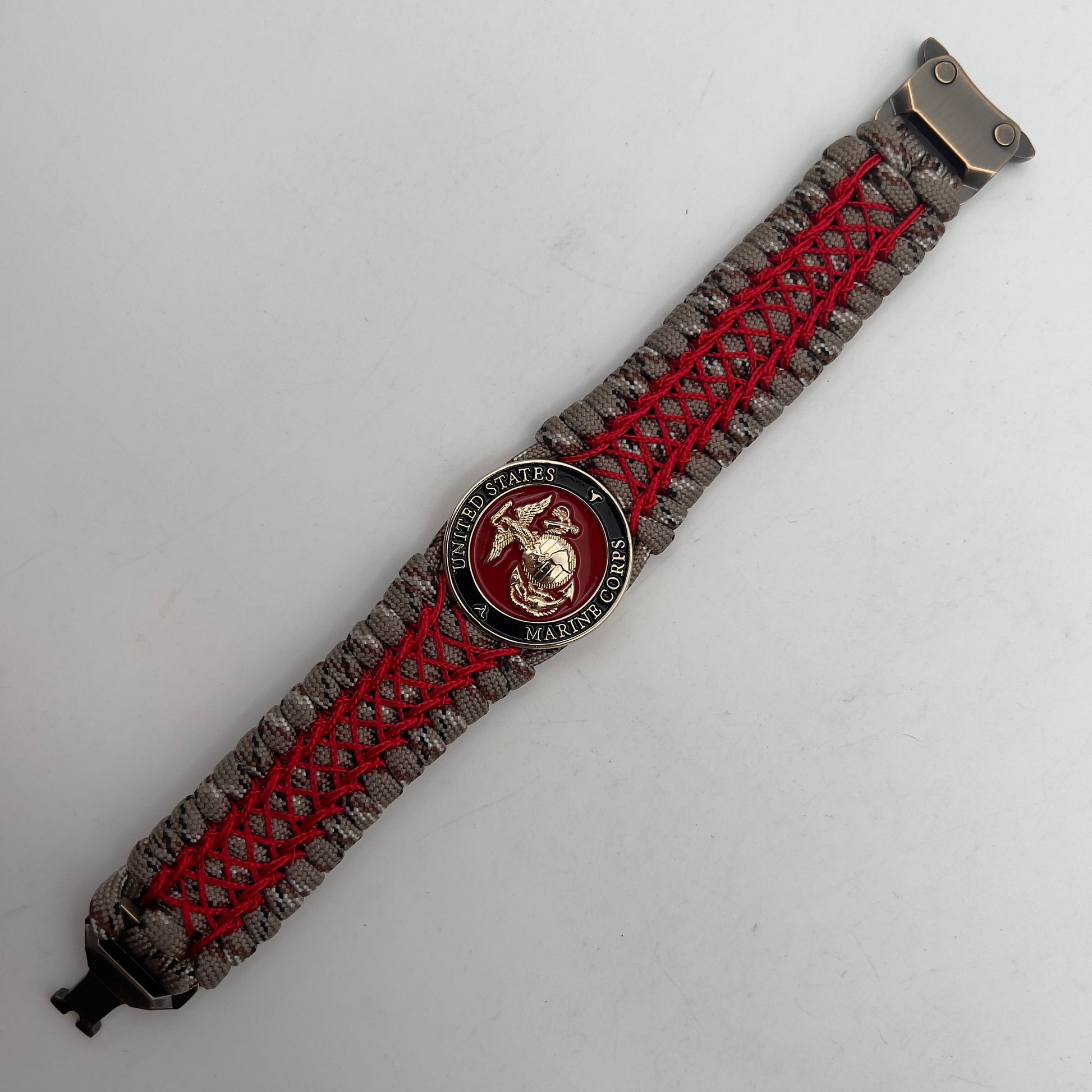 Thick, wide, rigid and comfortable braided United States Marine Corps bracelet featuring a 24K gold plated USMC Eagle Globe and Anchor medallion, a gold Cobra style tactical buckle and woven with Desert Camo 550 paracord and Imperial Red nano and micro cord.