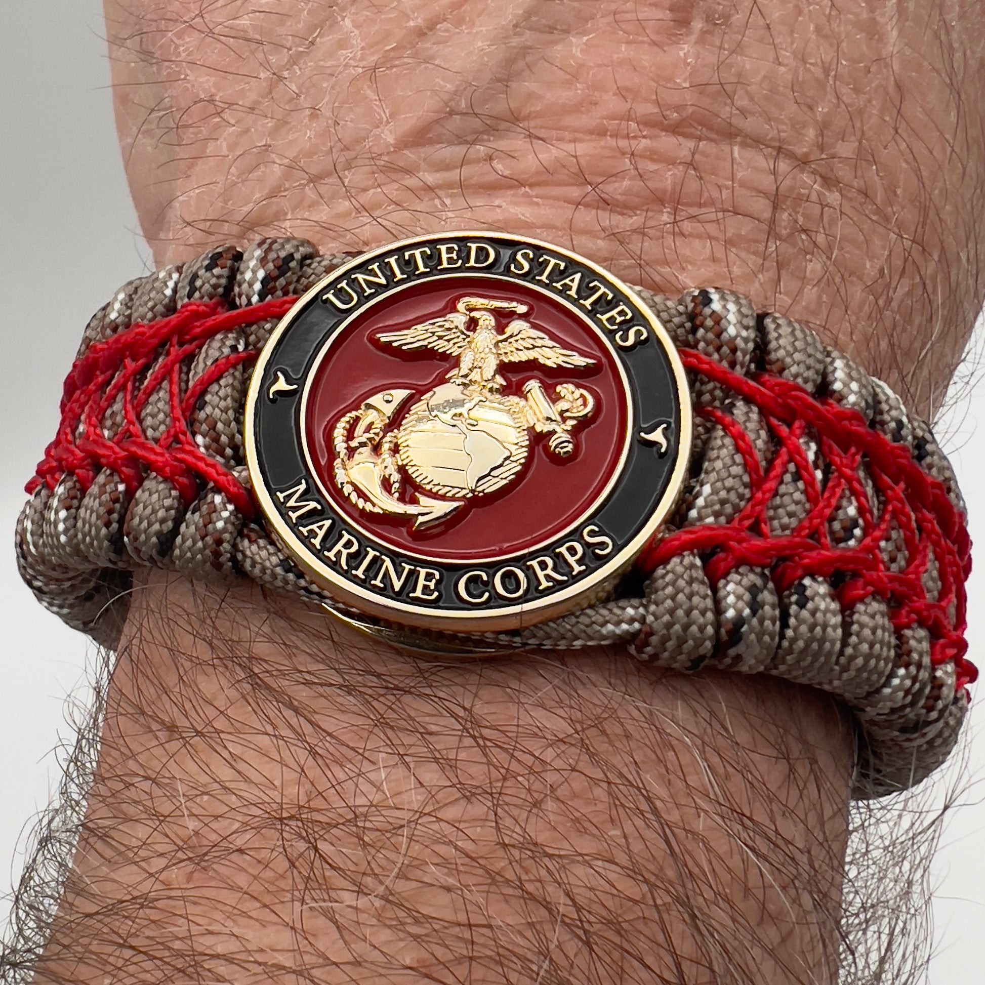 Thick, wide, rigid and comfortable braided United States Marine Corps bracelet featuring a 24K gold plated USMC Eagle Globe and Anchor medallion, a gold Cobra style tactical buckle and woven with Desert Camo 550 paracord and Imperial Red nano and micro cord.