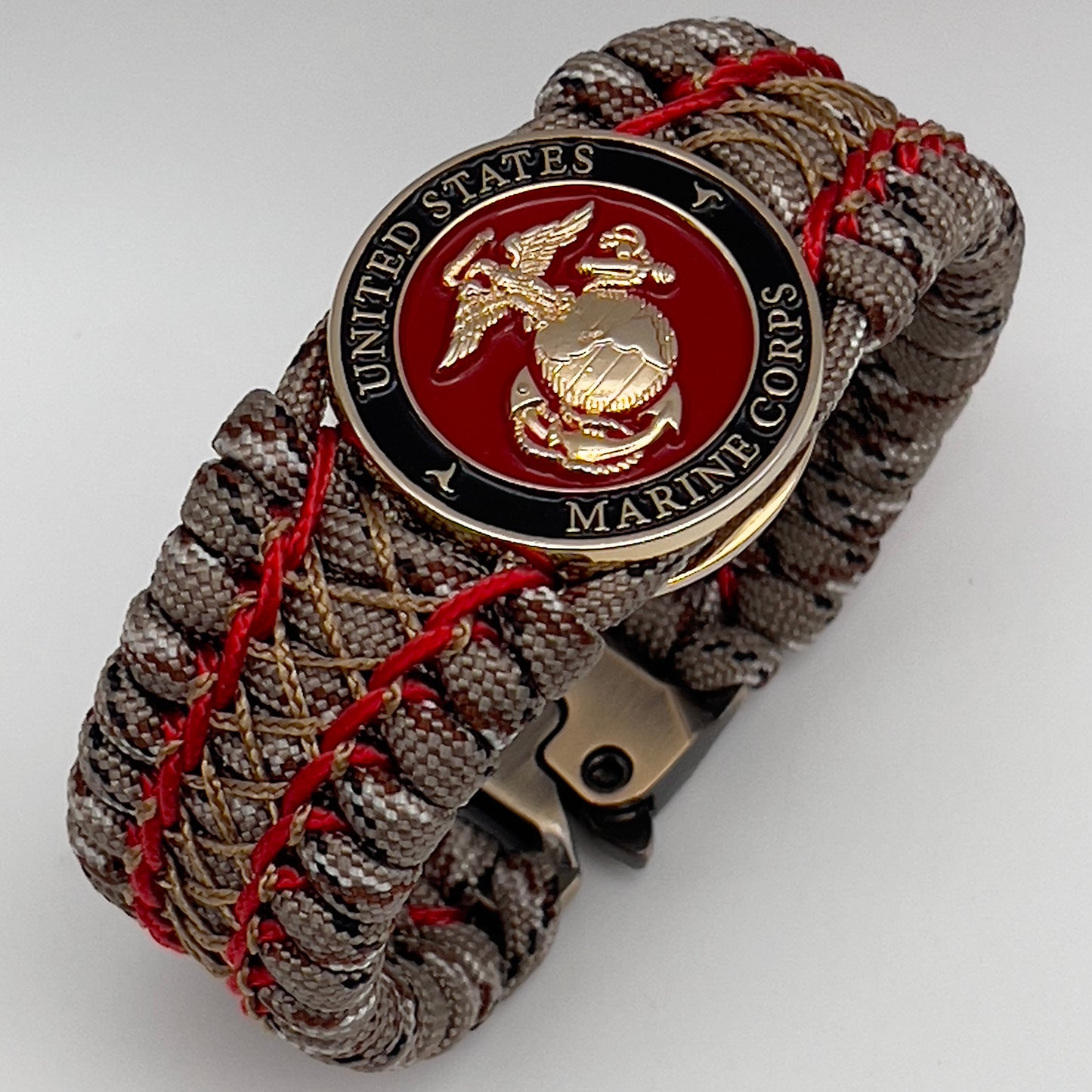 Thick, wide, rigid and comfortable braided United States Marine Corps bracelet featuring a 24K gold plated USMC Eagle Globe and Anchor medallion, a gold Cobra style tactical buckle and woven with Desert Camo 550 paracord and Imperial Red micro and gold nano cord.