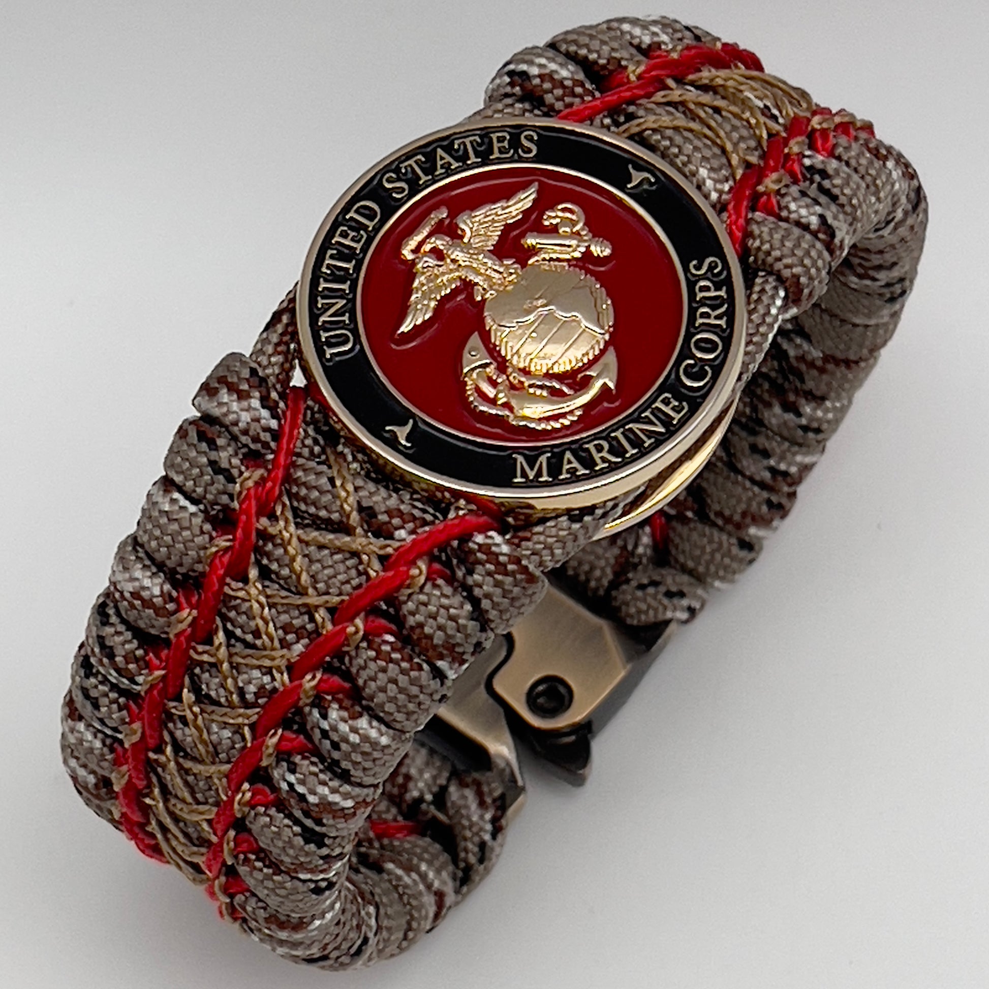 Thick, wide, rigid and comfortable braided United States Marine Corps bracelet featuring a 24K gold plated USMC Eagle Globe and Anchor medallion, a gold Cobra style tactical buckle and woven with Desert Camo 550 paracord and Imperial Red micro and gold nano cord.