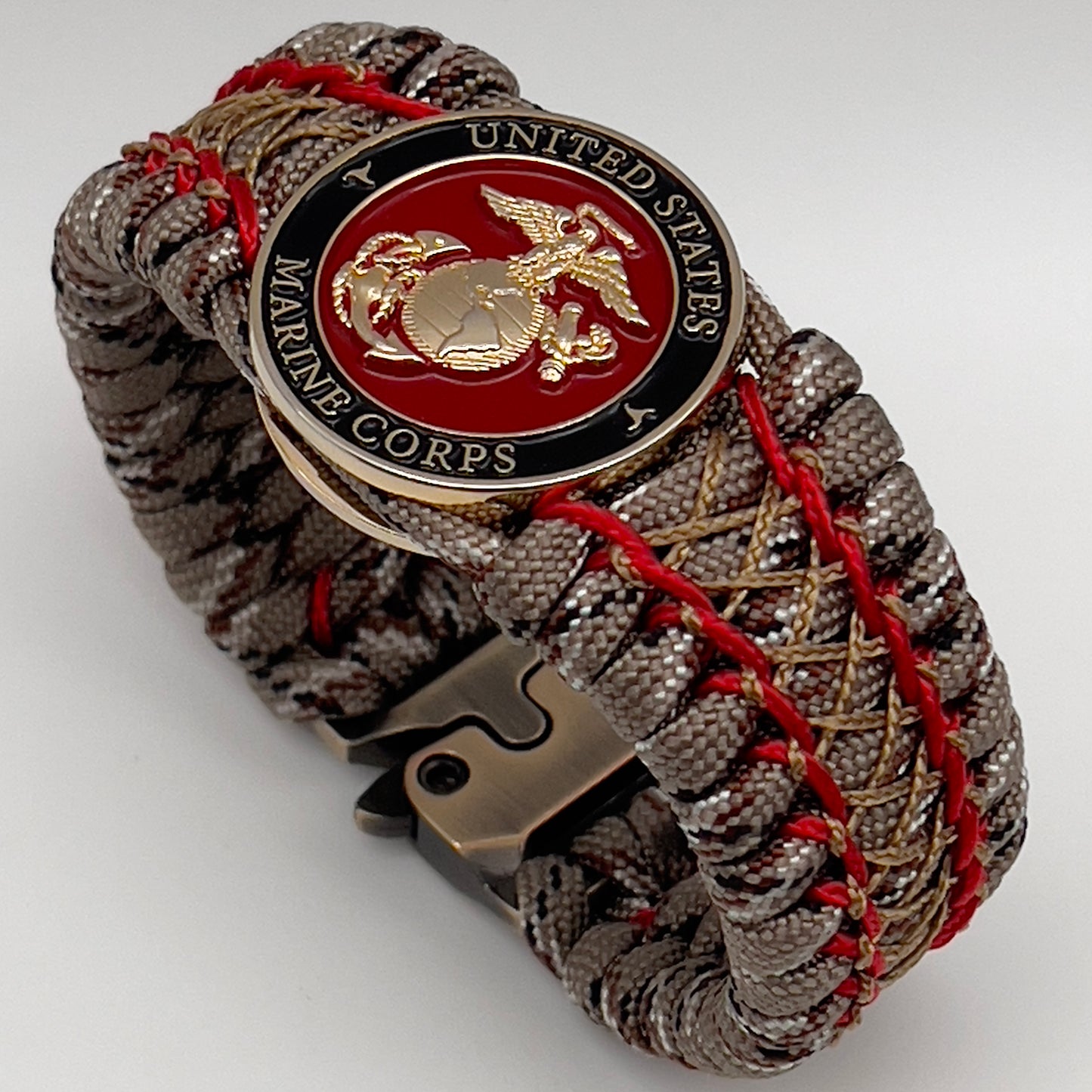 Thick, wide, rigid and comfortable braided United States Marine Corps bracelet featuring a 24K gold plated USMC Eagle Globe and Anchor medallion, a gold Cobra style tactical buckle and woven with Desert Camo 550 paracord and Imperial Red micro and gold nano cord.