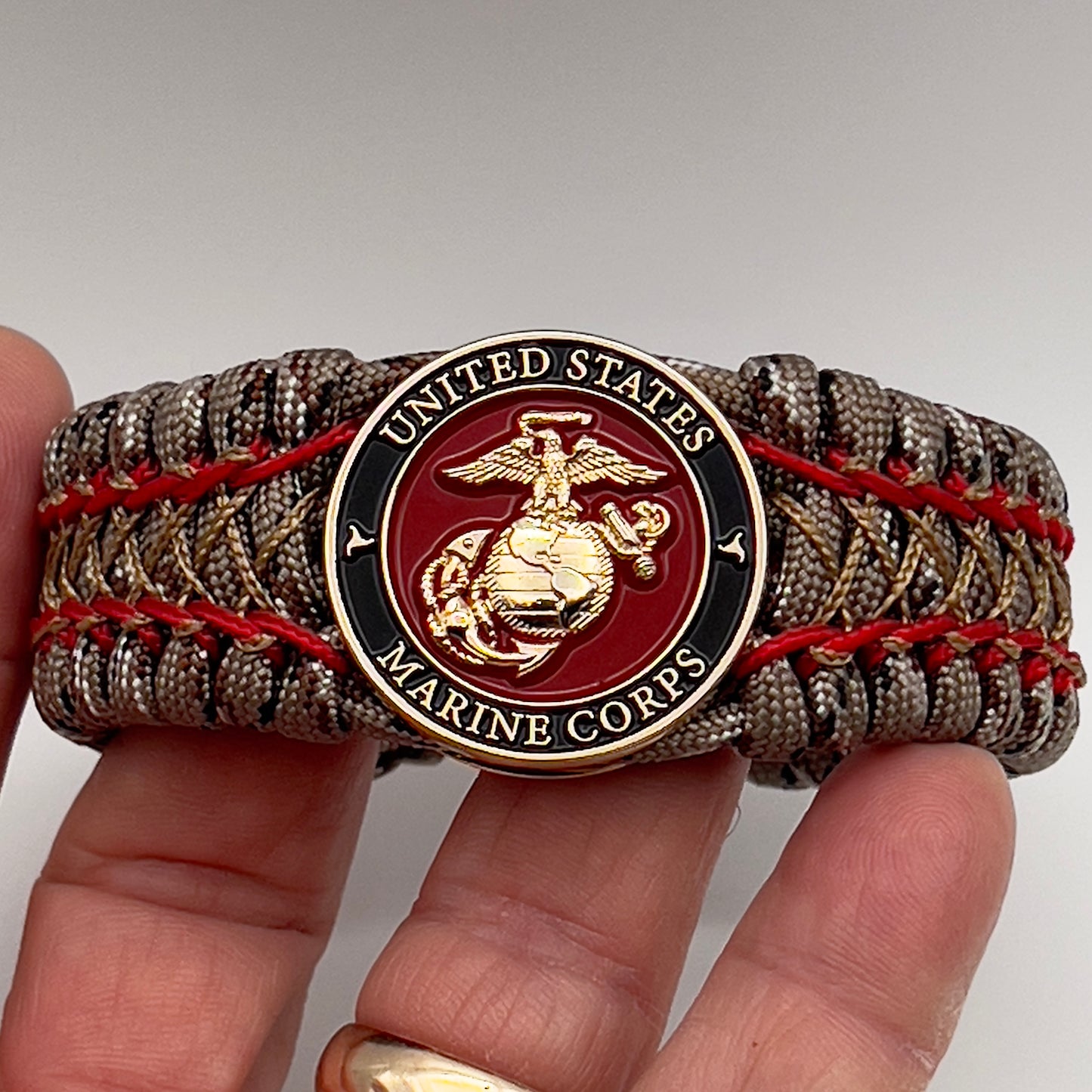Thick, wide, rigid and comfortable braided United States Marine Corps bracelet featuring a 24K gold plated USMC Eagle Globe and Anchor medallion, a gold Cobra style tactical buckle and woven with Desert Camo 550 paracord and Imperial Red micro and gold nano cord.