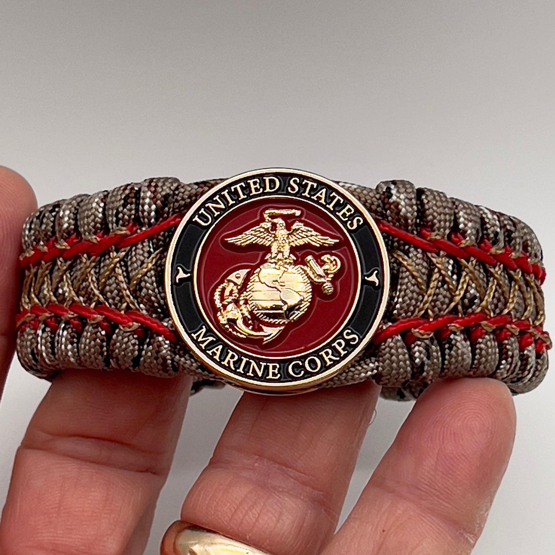 Thick, wide, rigid and comfortable braided United States Marine Corps bracelet featuring a 24K gold plated USMC Eagle Globe and Anchor medallion, a gold Cobra style tactical buckle and woven with Desert Camo 550 paracord and Imperial Red micro and gold nano cord.
