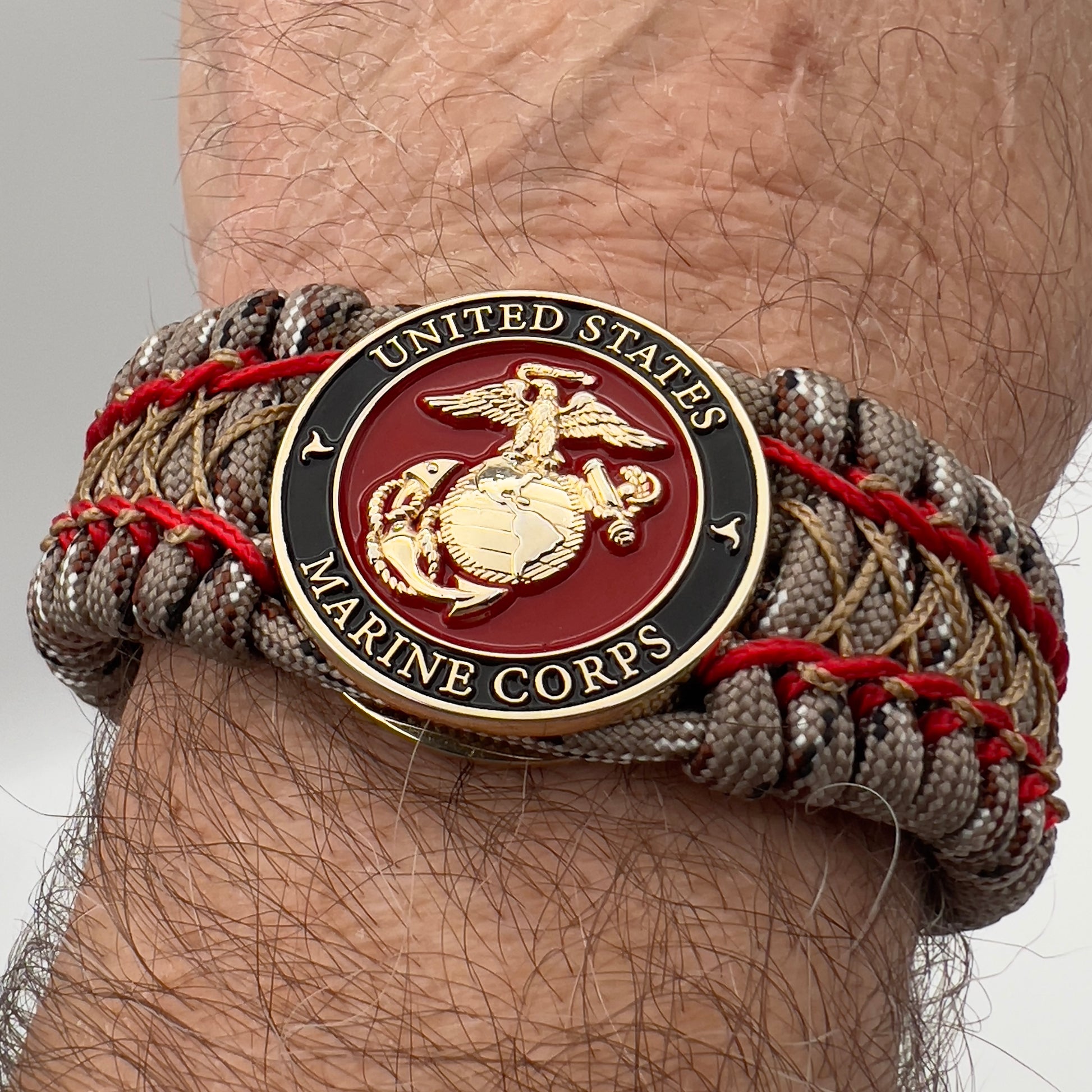 Thick, wide, rigid and comfortable braided United States Marine Corps bracelet featuring a 24K gold plated USMC Eagle Globe and Anchor medallion, a gold Cobra style tactical buckle and woven with Desert Camo 550 paracord and Imperial Red micro and gold nano cord.