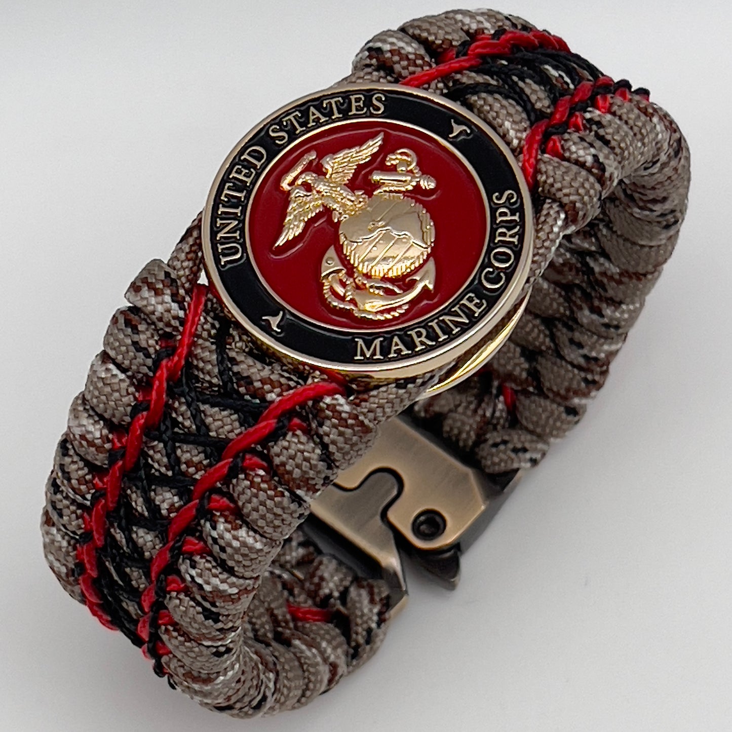 Thick, wide, rigid and comfortable braided United States Marine Corps bracelet featuring a 24K gold plated USMC Eagle Globe and Anchor medallion, a gold Cobra style tactical buckle and woven with Desert Camo 550 paracord, Imperial Red micro cord and black nano cord.