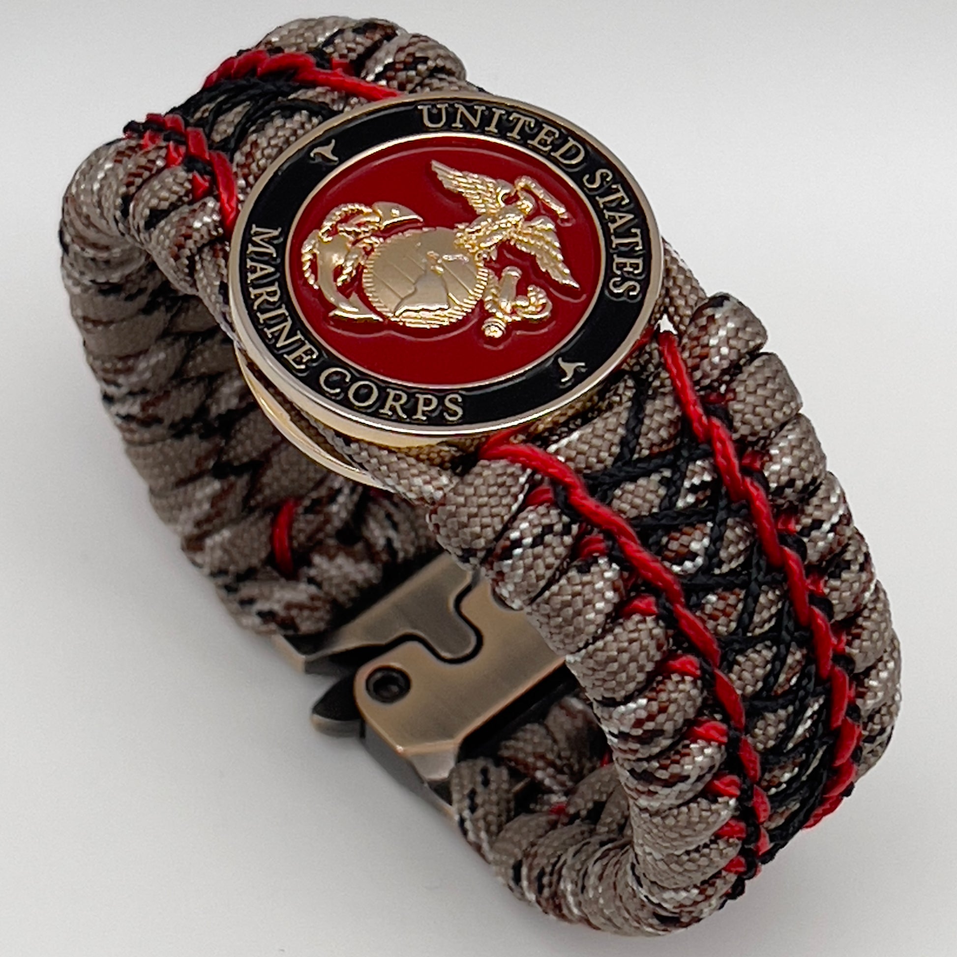Thick, wide, rigid and comfortable braided United States Marine Corps bracelet featuring a 24K gold plated USMC Eagle Globe and Anchor medallion, a gold Cobra style tactical buckle and woven with Desert Camo 550 paracord, Imperial Red micro cord and black nano cord.