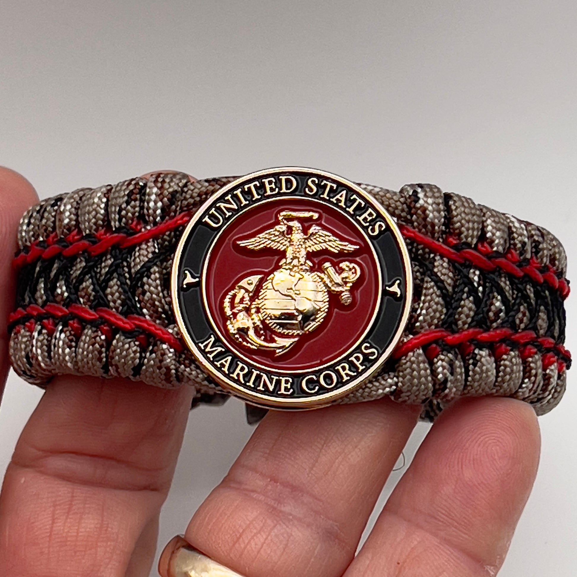 Thick, wide, rigid and comfortable braided United States Marine Corps bracelet featuring a 24K gold plated USMC Eagle Globe and Anchor medallion, a gold Cobra style tactical buckle and woven with Desert Camo 550 paracord, Imperial Red micro cord and black nano cord.