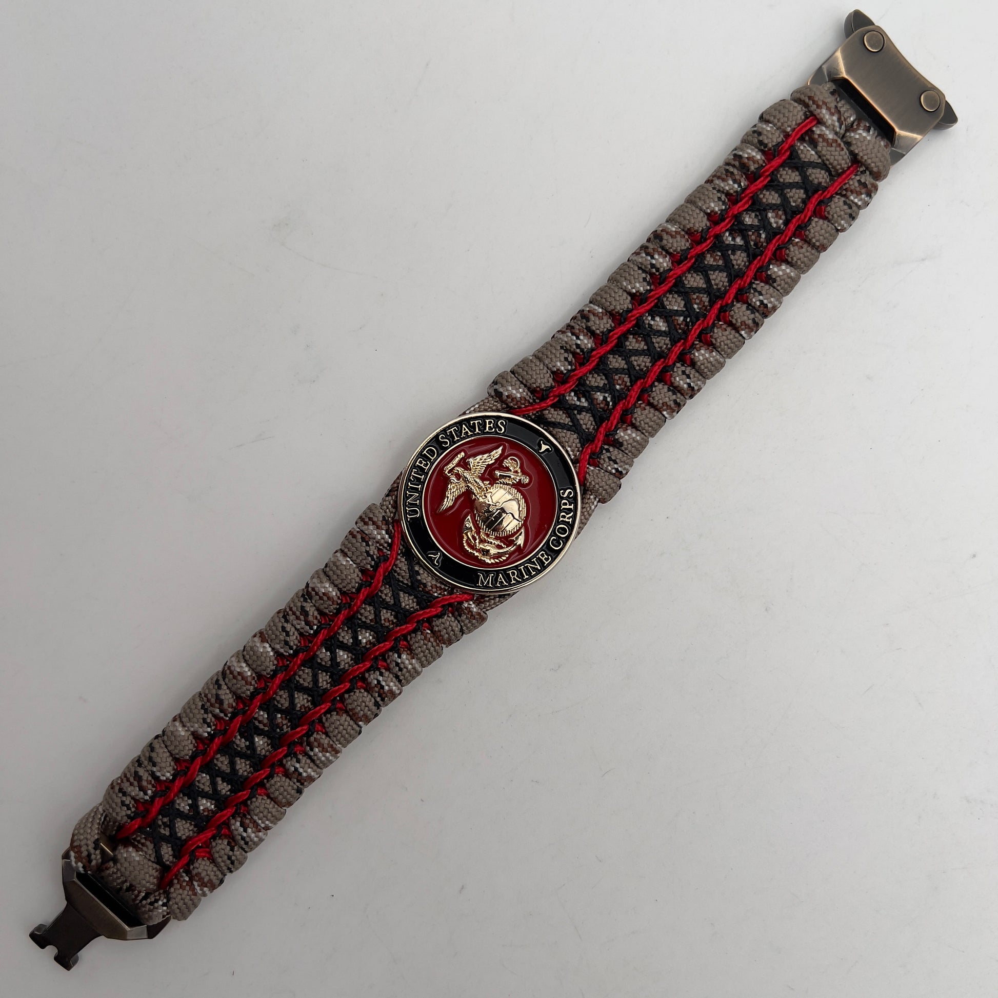 Thick, wide, rigid and comfortable braided United States Marine Corps bracelet featuring a 24K gold plated USMC Eagle Globe and Anchor medallion, a gold Cobra style tactical buckle and woven with Desert Camo 550 paracord, Imperial Red micro cord and black nano cord.