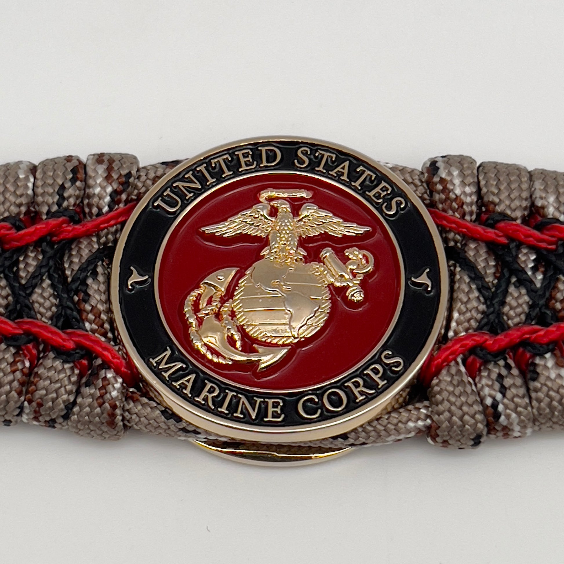 Thick, wide, rigid and comfortable braided United States Marine Corps bracelet featuring a 24K gold plated USMC Eagle Globe and Anchor medallion, a gold Cobra style tactical buckle and woven with Desert Camo 550 paracord, Imperial Red micro cord and black nano cord.
