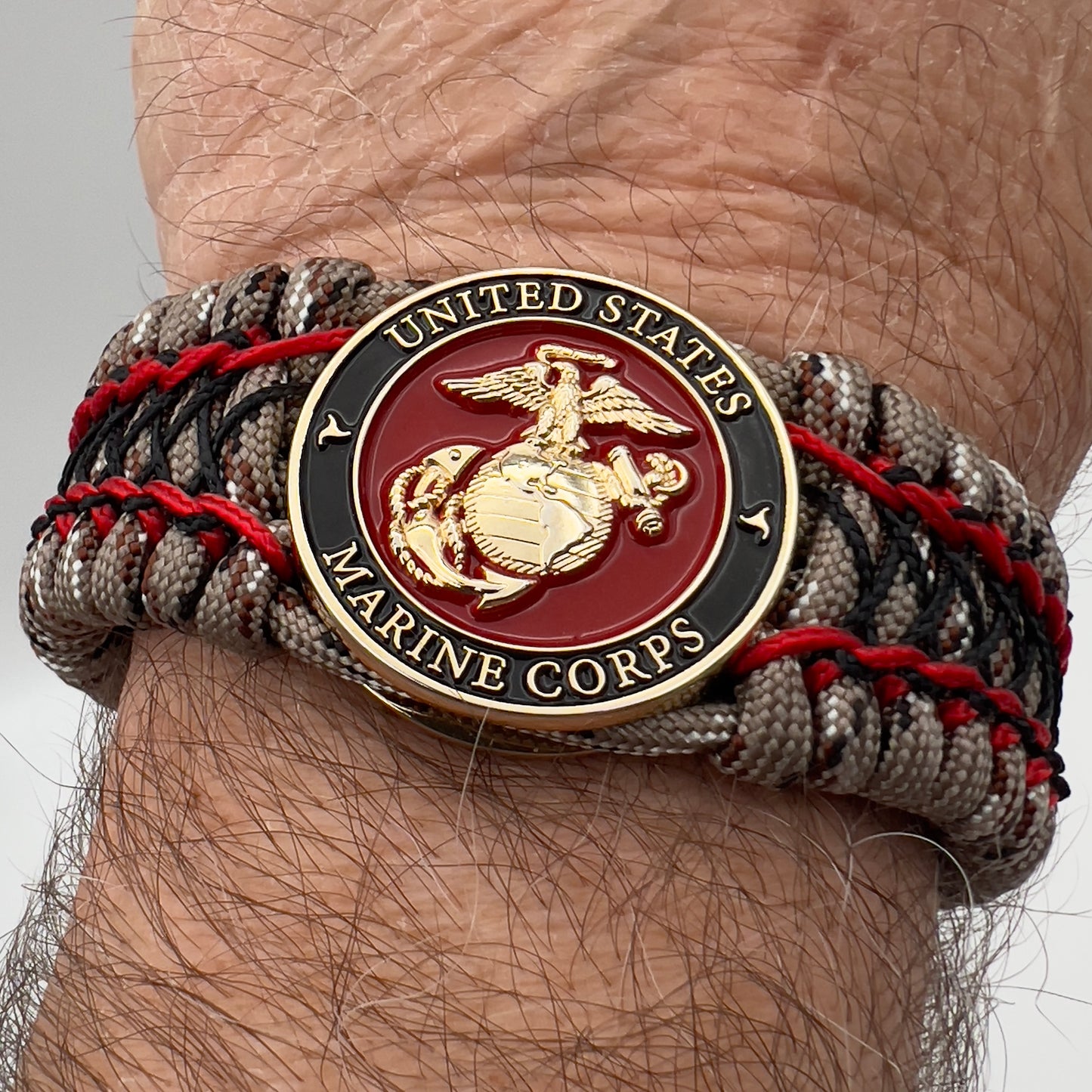 Thick, wide, rigid and comfortable braided United States Marine Corps bracelet featuring a 24K gold plated USMC Eagle Globe and Anchor medallion, a gold Cobra style tactical buckle and woven with Desert Camo 550 paracord, Imperial Red micro cord and black nano cord.