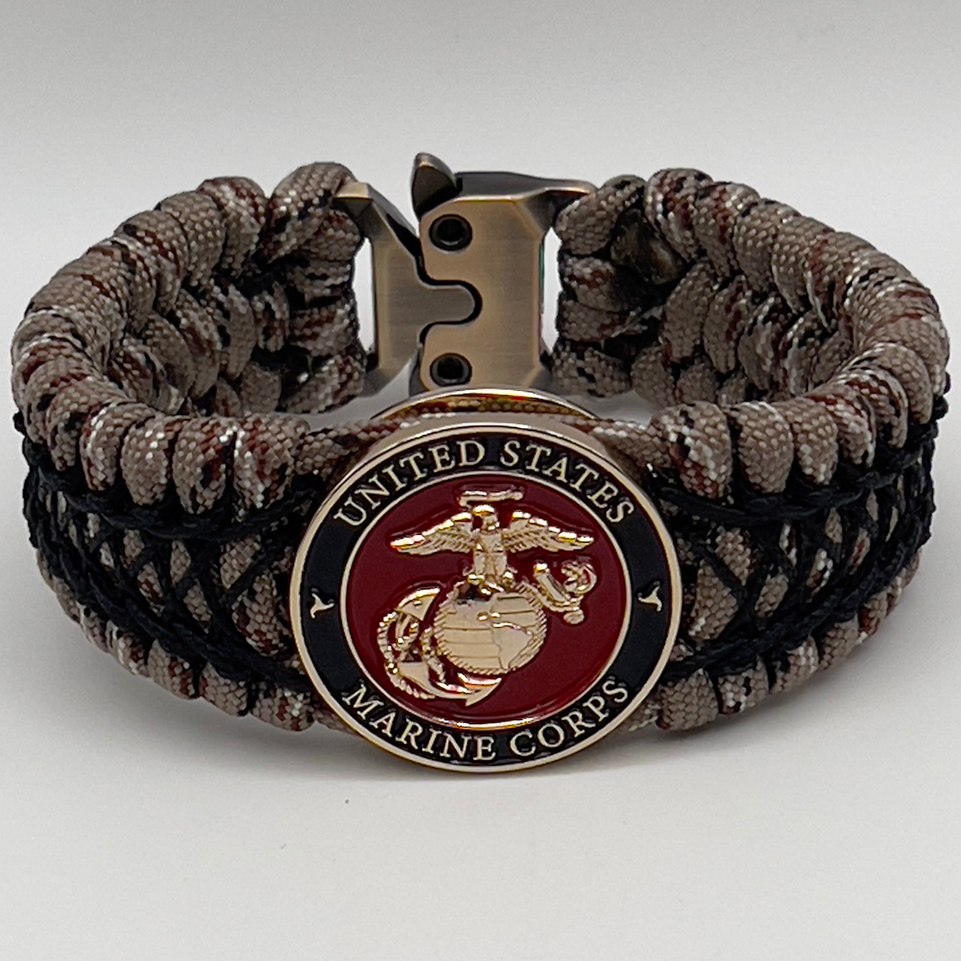 Thick, wide, rigid and comfortable braided United States Marine Corps bracelet featuring a 24K gold plated USMC Eagle Globe and Anchor medallion, a gold Cobra style tactical buckle and woven with Desert Camo 550 paracord and black nano and micro cord.