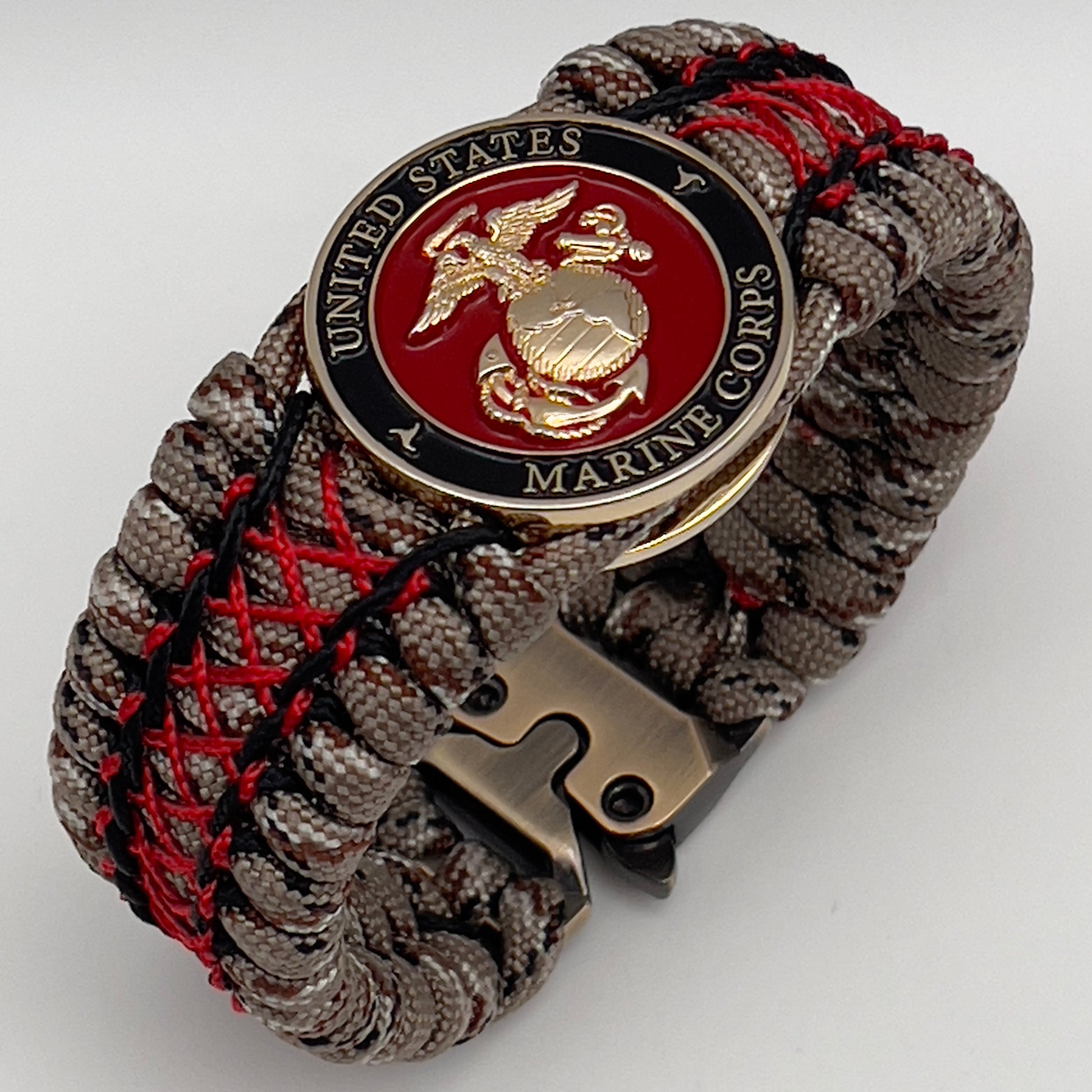 Thick, wide, rigid and comfortable braided United States Marine Corps bracelet featuring a 24K gold plated USMC Eagle Globe and Anchor medallion, a gold Cobra style tactical buckle and woven with Desert Camo 550 paracord, black micro cord and Imperial Red nano cord.