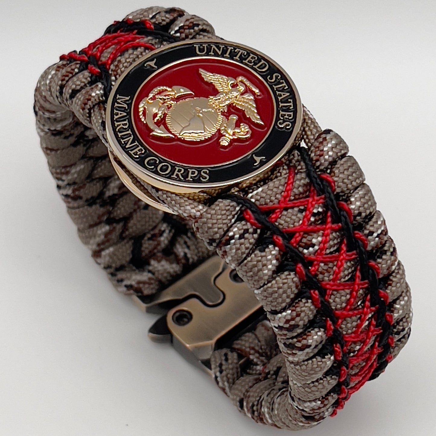 Thick, wide, rigid and comfortable braided United States Marine Corps bracelet featuring a 24K gold plated USMC Eagle Globe and Anchor medallion, a gold Cobra style tactical buckle and woven with Desert Camo 550 paracord, black micro cord and Imperial Red nano cord.