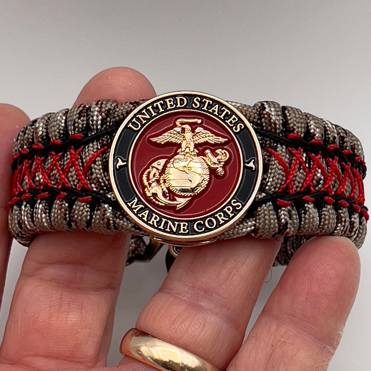 Thick, wide, rigid and comfortable braided United States Marine Corps bracelet featuring a 24K gold plated USMC Eagle Globe and Anchor medallion, a gold Cobra style tactical buckle and woven with Desert Camo 550 paracord, black micro cord and Imperial Red nano cord.