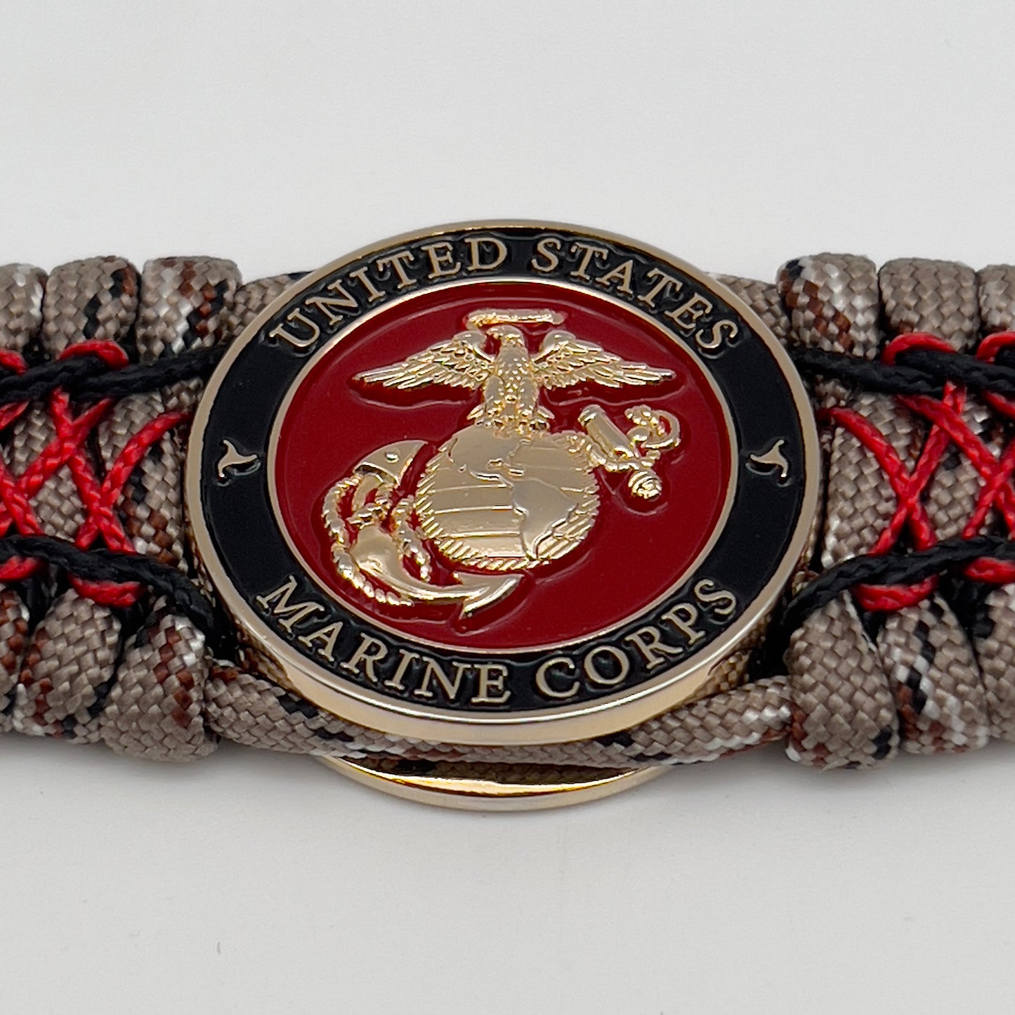 Thick, wide, rigid and comfortable braided United States Marine Corps bracelet featuring a 24K gold plated USMC Eagle Globe and Anchor medallion, a gold Cobra style tactical buckle and woven with Desert Camo 550 paracord, black micro cord and Imperial Red nano cord.