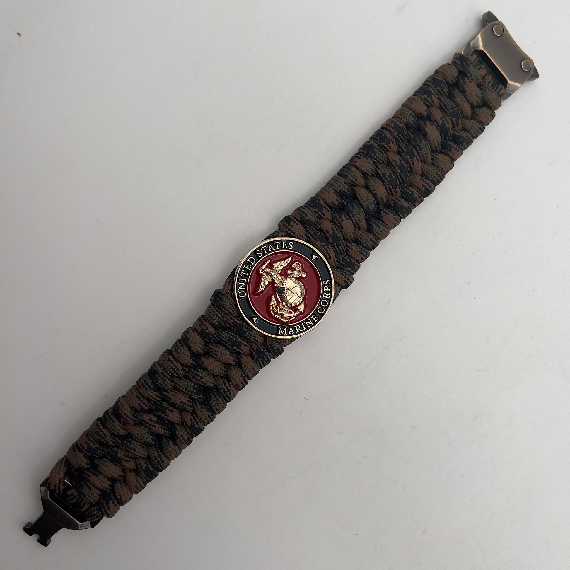 Thick, wide, semi-rigid and comfortable braided United States Marine Corps bracelet featuring a 24K gold plated USMC Eagle Globe and Anchor medallion, a gold Cobra style tactical buckle and woven with Woodland Camo 550 paracord.