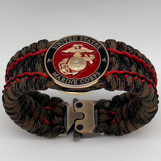 Thick, wide, rigid and comfortable braided United States Marine Corps bracelet featuring a 24K gold plated USMC Eagle Globe and Anchor medallion, a gold Cobra style tactical buckle and woven with Woodland Camo 550 paracord and Imperial Red micro and black nano cord.