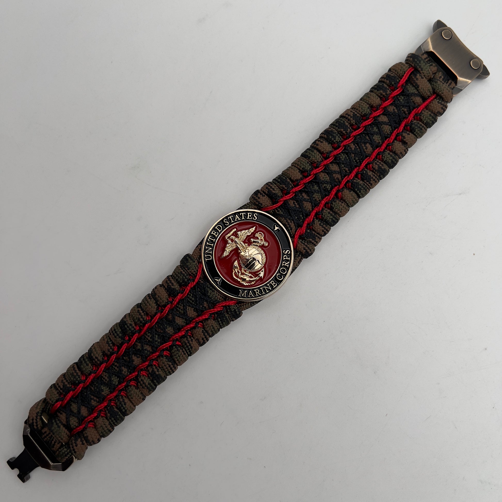 Thick, wide, rigid and comfortable braided United States Marine Corps bracelet featuring a 24K gold plated USMC Eagle Globe and Anchor medallion, a gold Cobra style tactical buckle and woven with Woodland Camo 550 paracord and Imperial Red micro and black nano cord.