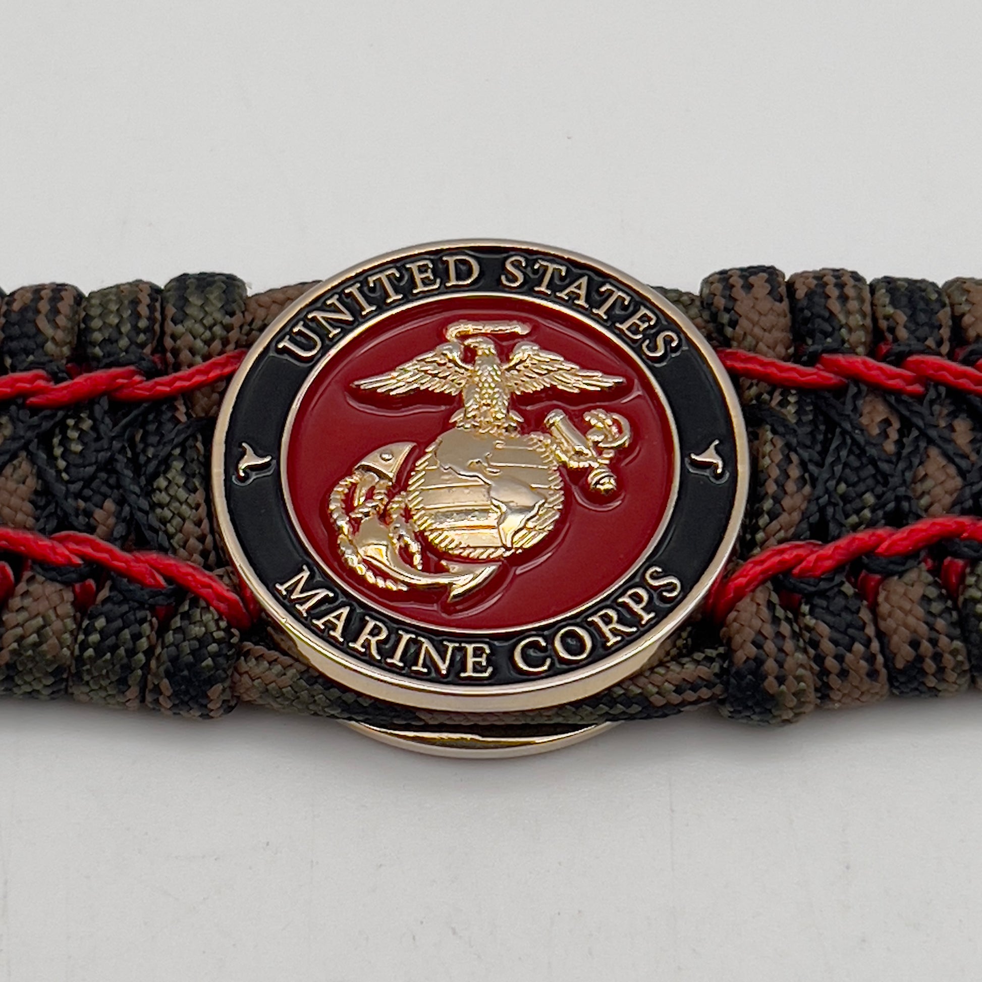 Thick, wide, rigid and comfortable braided United States Marine Corps bracelet featuring a 24K gold plated USMC Eagle Globe and Anchor medallion, a gold Cobra style tactical buckle and woven with Woodland Camo 550 paracord and Imperial Red micro and black nano cord.