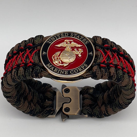 Thick, wide, rigid and comfortable braided United States Marine Corps bracelet featuring a 24K gold plated USMC Eagle Globe and Anchor medallion, a gold Cobra style tactical buckle and woven with Woodland Camo 550 paracord and Imperial Red micro and black nano cord.