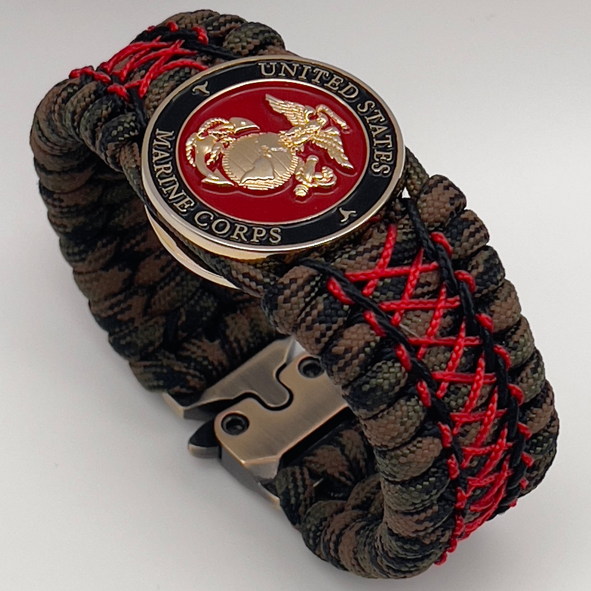 Thick, wide, rigid and comfortable braided United States Marine Corps bracelet featuring a 24K gold plated USMC Eagle Globe and Anchor medallion, a gold Cobra style tactical buckle and woven with Woodland Camo 550 paracord and Imperial Red micro and black nano cord.