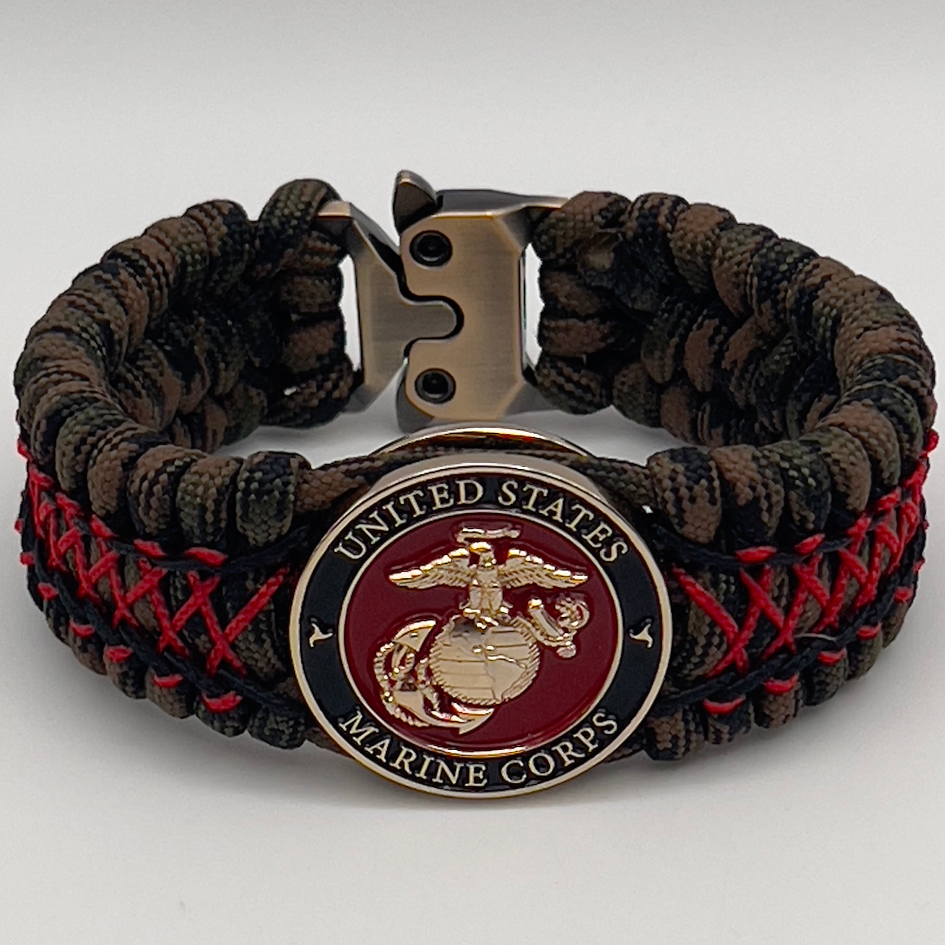 Thick, wide, rigid and comfortable braided United States Marine Corps bracelet featuring a 24K gold plated USMC Eagle Globe and Anchor medallion, a gold Cobra style tactical buckle and woven with Woodland Camo 550 paracord and Imperial Red micro and black nano cord.
