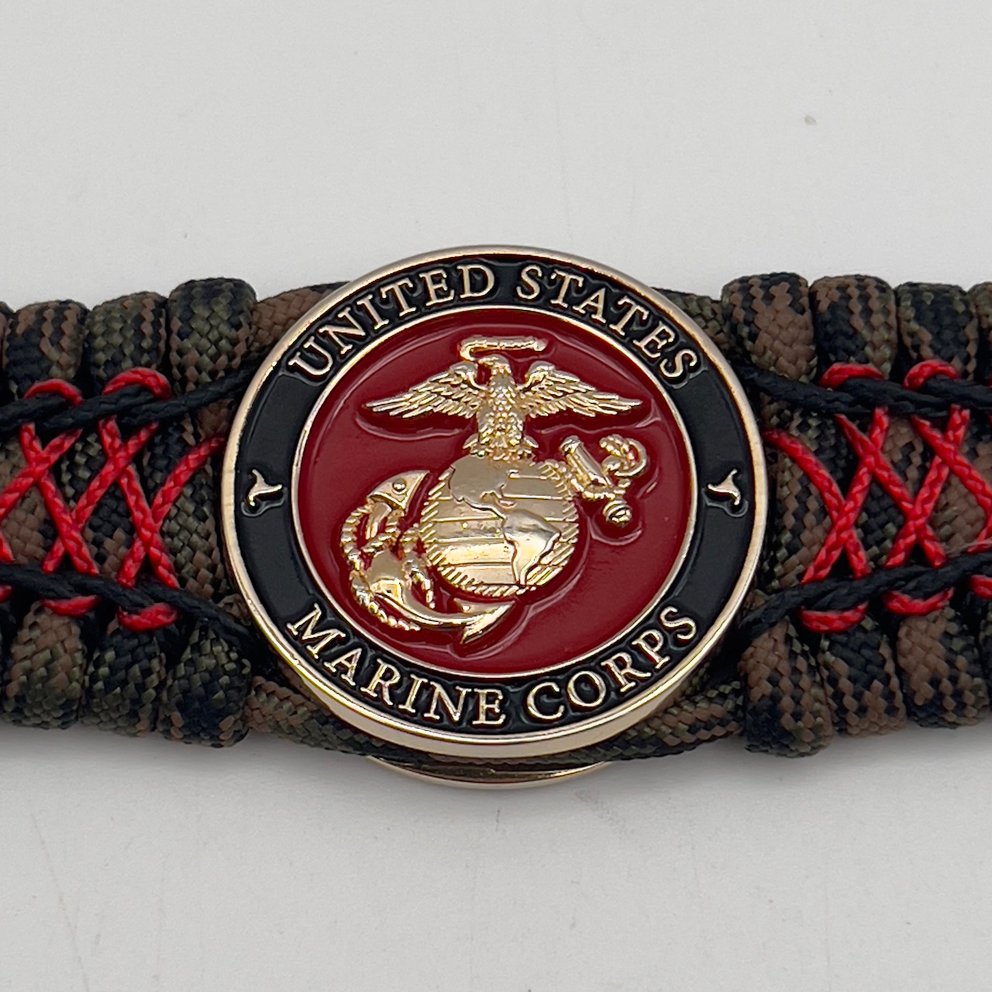 Thick, wide, rigid and comfortable braided United States Marine Corps bracelet featuring a 24K gold plated USMC Eagle Globe and Anchor medallion, a gold Cobra style tactical buckle and woven with Woodland Camo 550 paracord and Imperial Red micro and black nano cord.