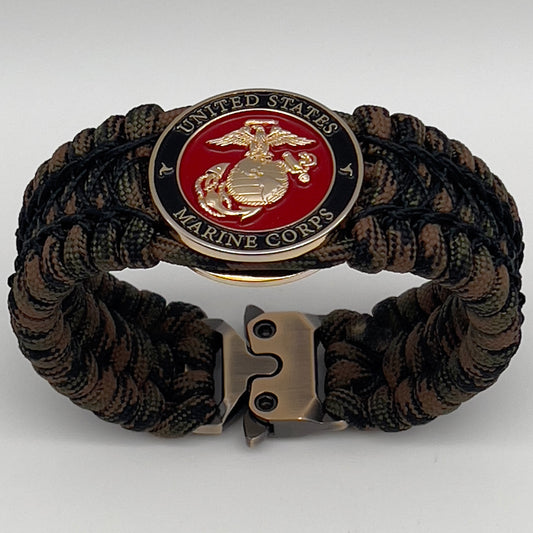 Thick, wide, rigid and comfortable braided United States Marine Corps bracelet featuring a 24K gold plated USMC Eagle Globe and Anchor medallion, a gold Cobra style tactical buckle and woven with Woodland Camo 550 paracord and black nano and micro cord.