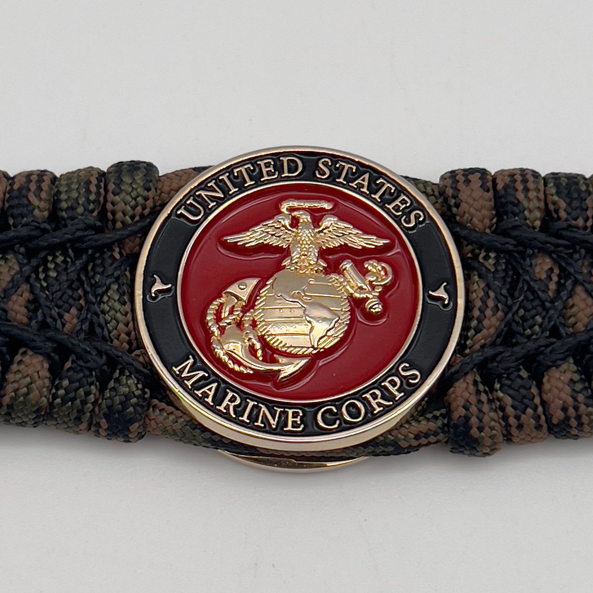 Thick, wide, rigid and comfortable braided United States Marine Corps bracelet featuring a 24K gold plated USMC Eagle Globe and Anchor medallion, a gold Cobra style tactical buckle and woven with Woodland Camo 550 paracord and black nano and micro cord.