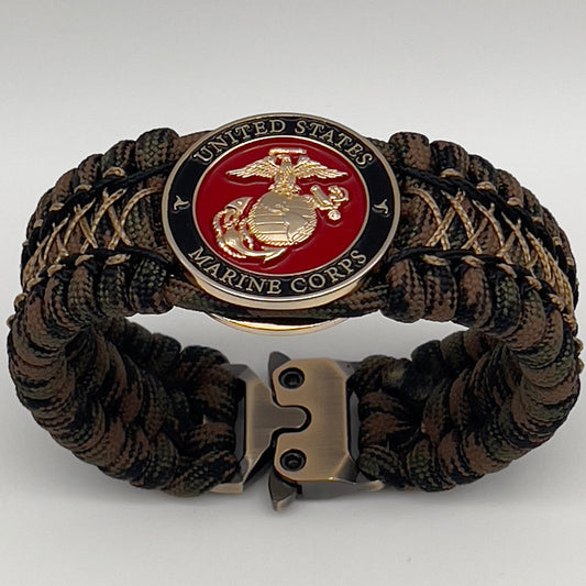 Thick, wide, rigid and comfortable braided United States Marine Corps bracelet featuring a 24K gold plated USMC Eagle Globe and Anchor medallion, a gold Cobra style tactical buckle and woven with Woodland 550 paracord, black micro and tan nano cord.