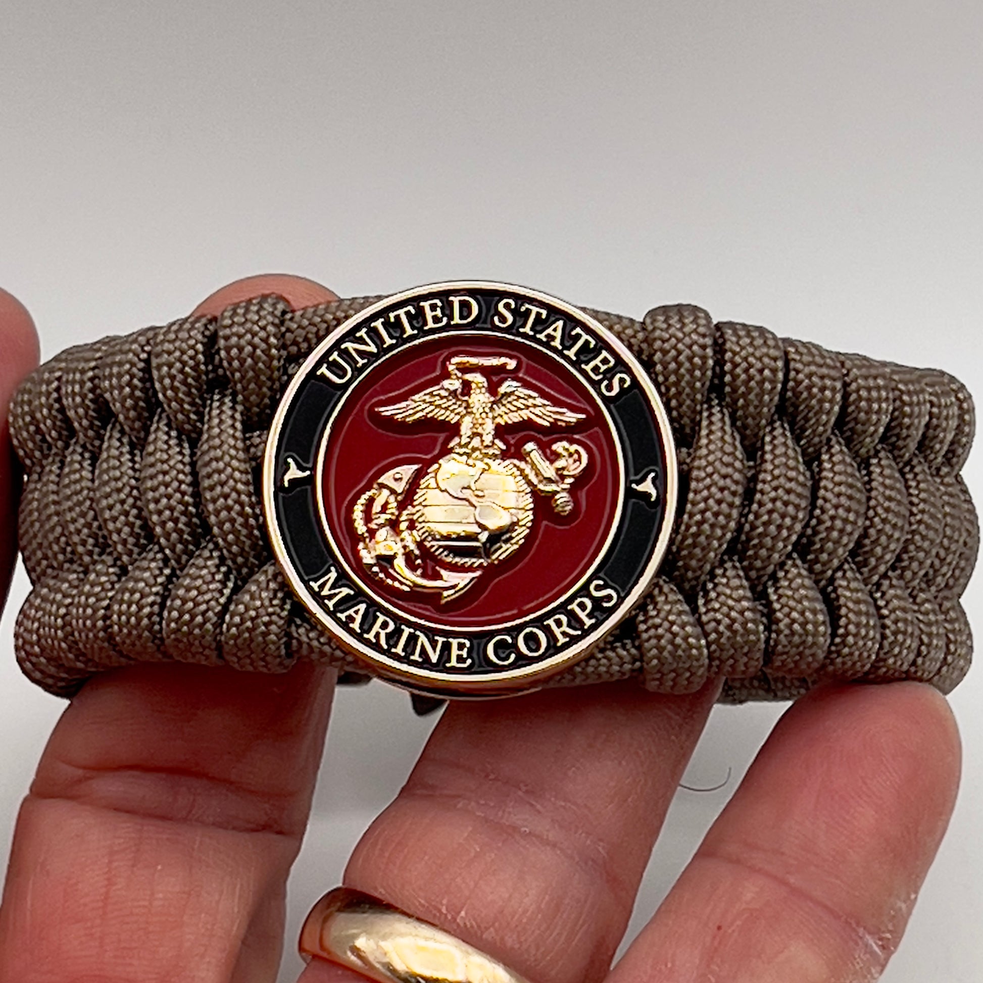 Thick, wide, semi-rigid and comfortable braided United States Marine Corps bracelet featuring a 24K gold plated USMC Eagle Globe and Anchor medallion, a gold Cobra style tactical buckle and woven with tan 550 paracord.