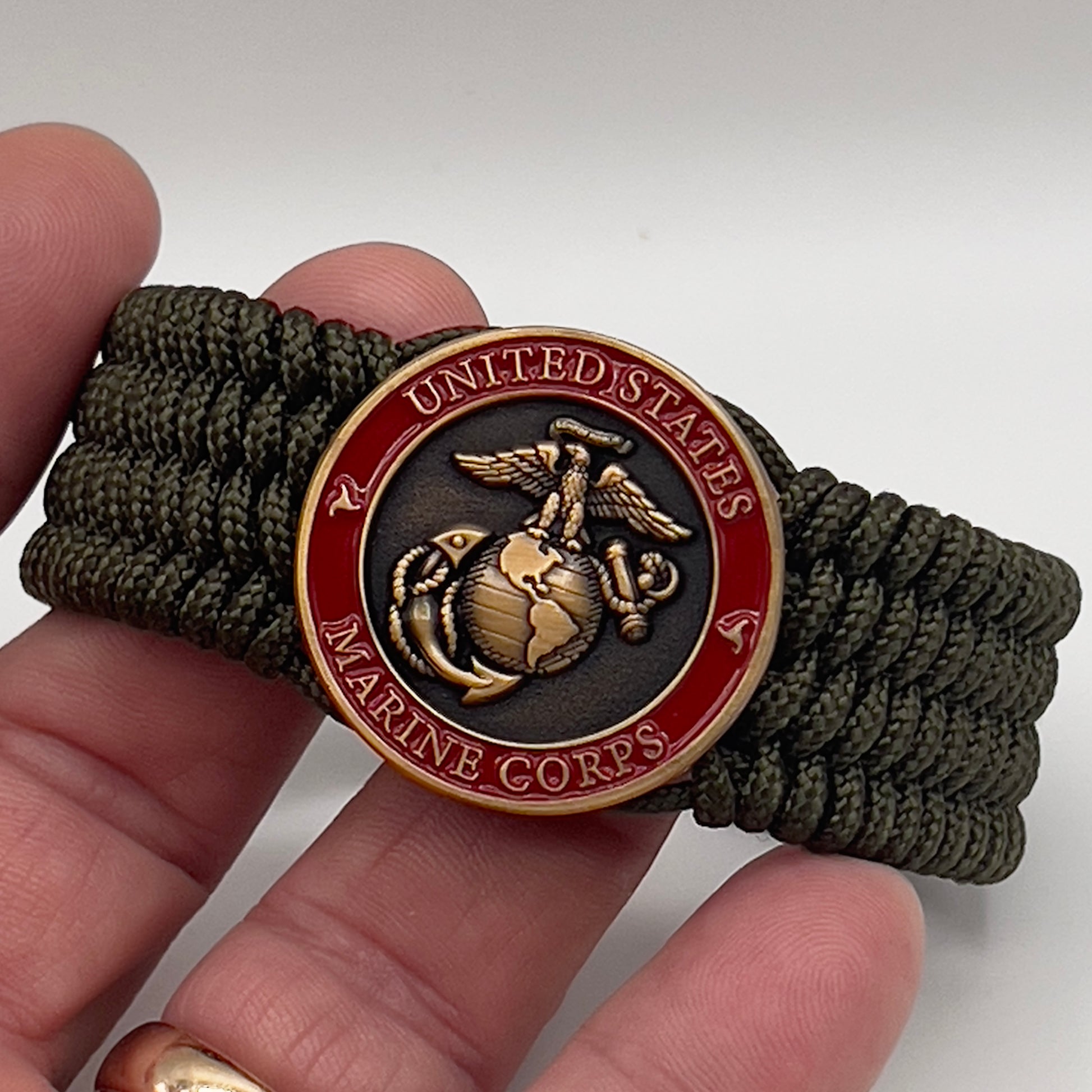 Thin, wide, very flexible and comfortable braided United States Marine Corps bracelet featuring a 24K antique gold plated USMC Eagle Globe and Anchor medallion, a gold Cobra style tactical buckle and woven with OIive Drab Type-1 paracord.