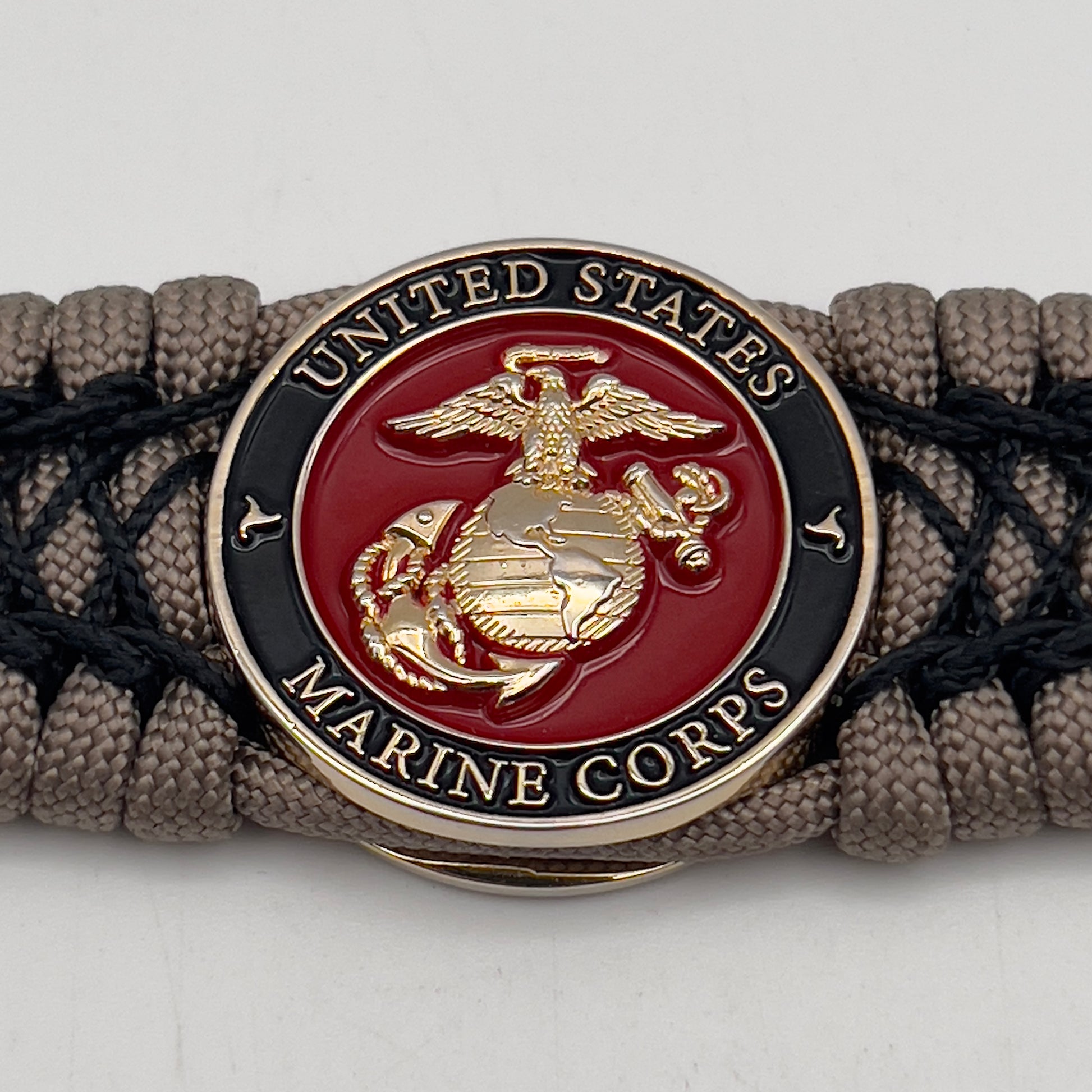 Thick, wide, rigid and comfortable braided United States Marine Corps bracelet featuring a 24K gold plated USMC Eagle Globe and Anchor medallion, a gold Cobra style tactical buckle and woven with tan 550 paracord and black nano and micro cord.