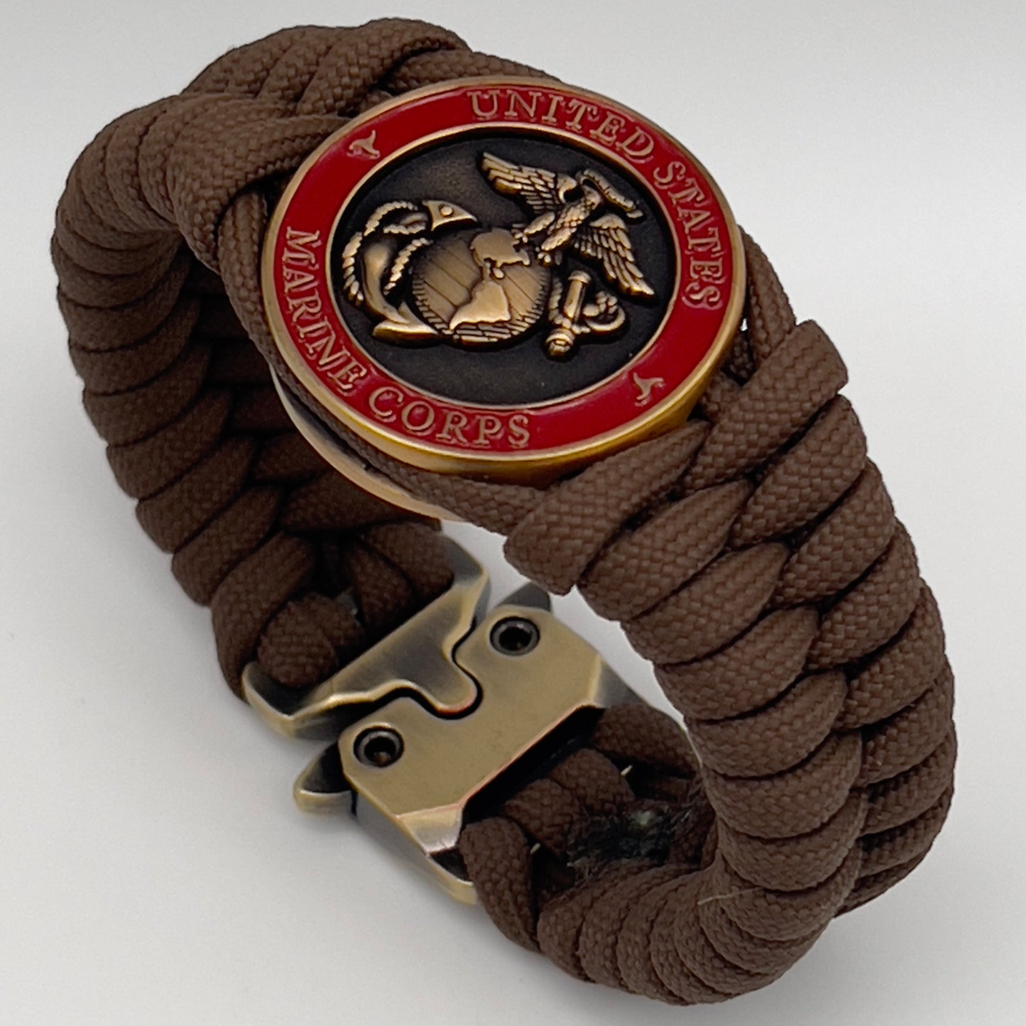 Thick, medium width, semi-rigid and comfortable braided United States Marine Corps bracelet featuring a 24K antique gold plated USMC Eagle Globe and Anchor medallion, a gold Cobra style tactical buckle and woven with Coyote Brown 550 paracord 