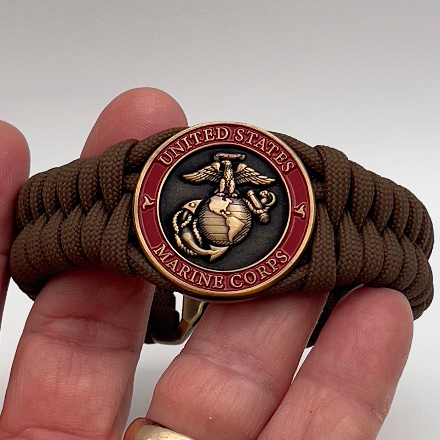 Thick, medium width, semi-rigid and comfortable braided United States Marine Corps bracelet featuring a 24K antique gold plated USMC Eagle Globe and Anchor medallion, a gold Cobra style tactical buckle and woven with Coyote Brown 550 paracord 