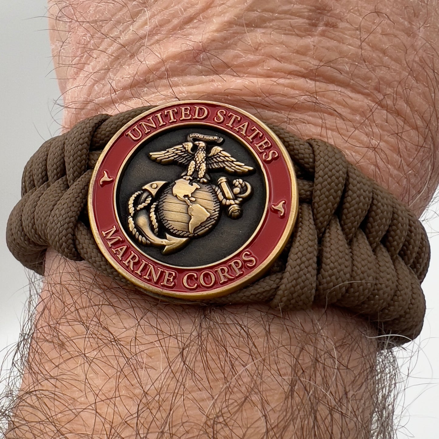 Thick, medium width, semi-rigid and comfortable braided United States Marine Corps bracelet featuring a 24K antique gold plated USMC Eagle Globe and Anchor medallion, a gold Cobra style tactical buckle and woven with Coyote Brown 550 paracord 