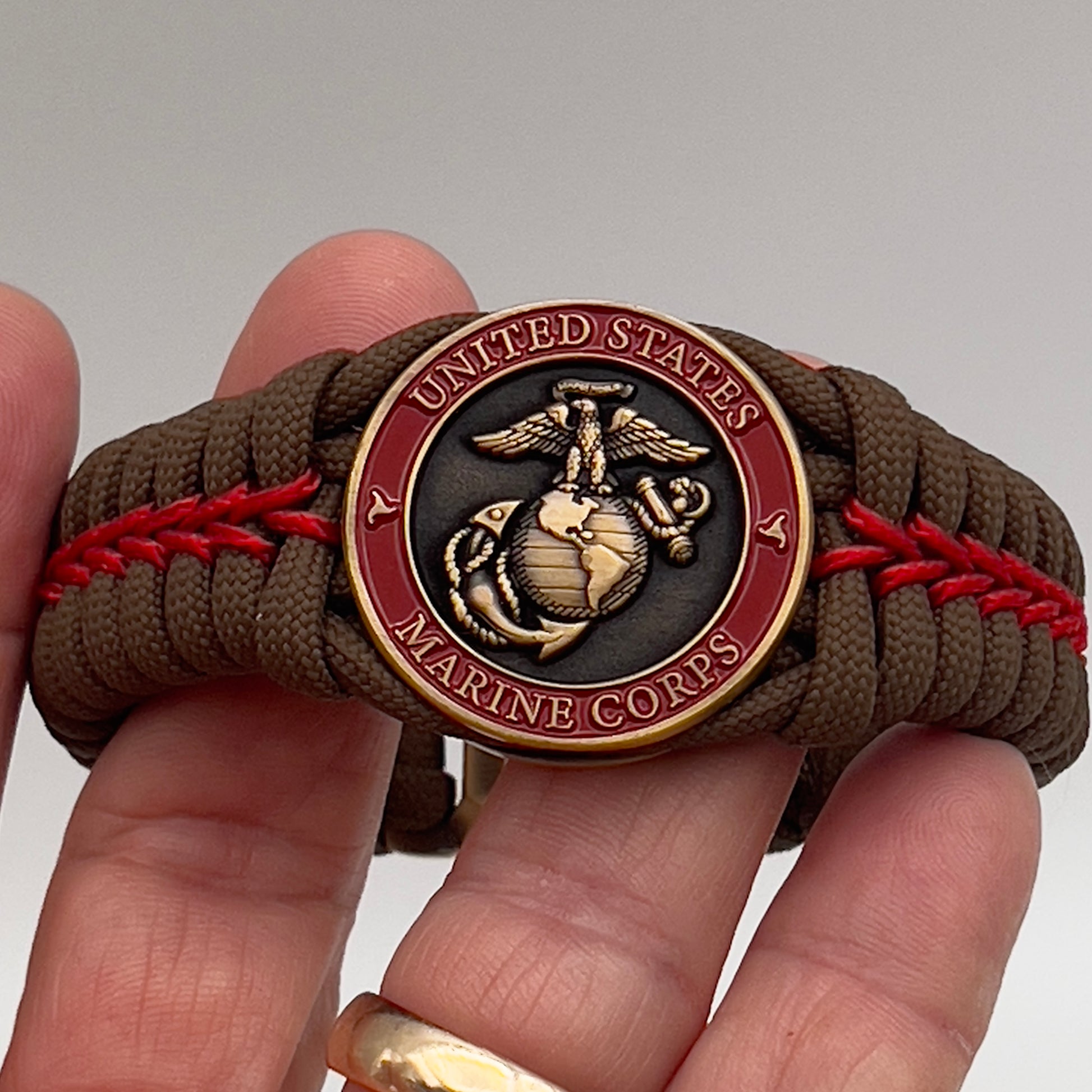 Thick, medium width, semi-rigid and comfortable braided United States Marine Corps bracelet featuring a 24K antique gold plated USMC Eagle Globe and Anchor medallion, a gold Cobra style tactical buckle and woven with Coyote Brown 550 paracord and Imperial Red micro cord.