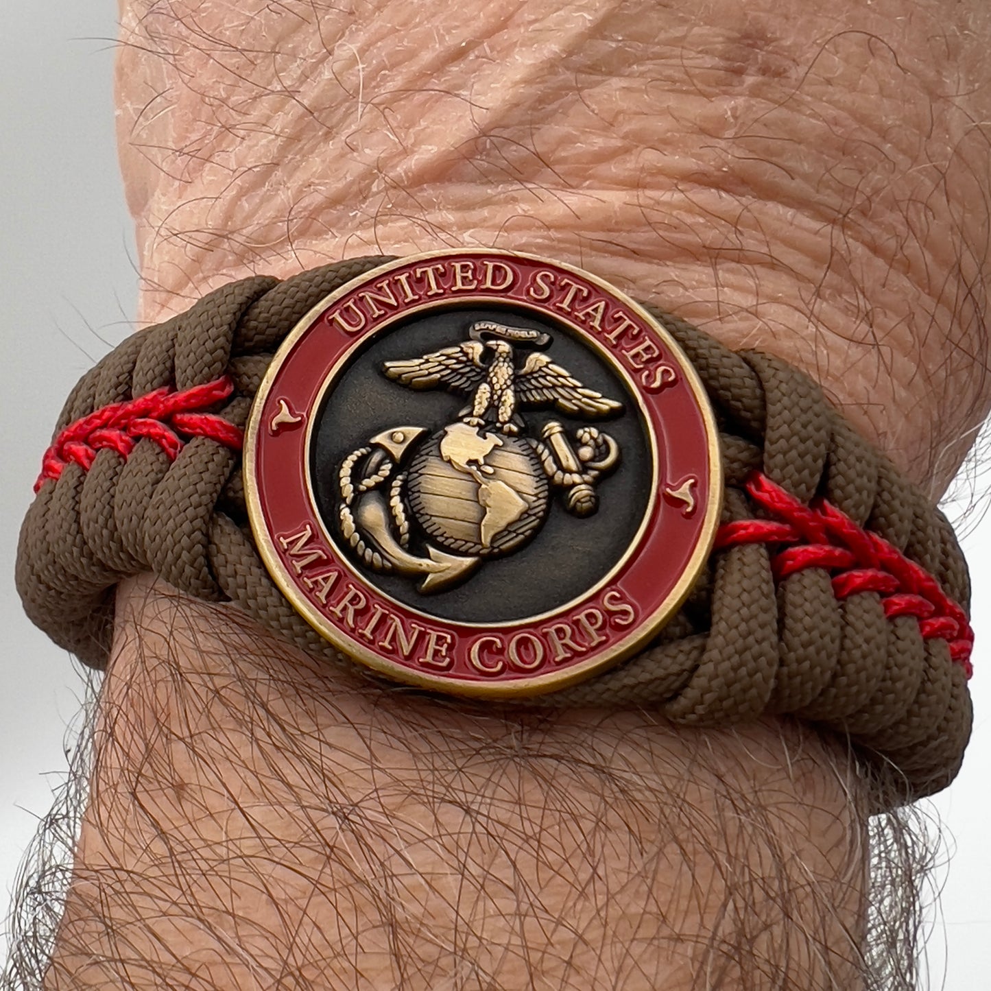 Thick, medium width, semi-rigid and comfortable braided United States Marine Corps bracelet featuring a 24K antique gold plated USMC Eagle Globe and Anchor medallion, a gold Cobra style tactical buckle and woven with Coyote Brown 550 paracord and Imperial Red micro cord.