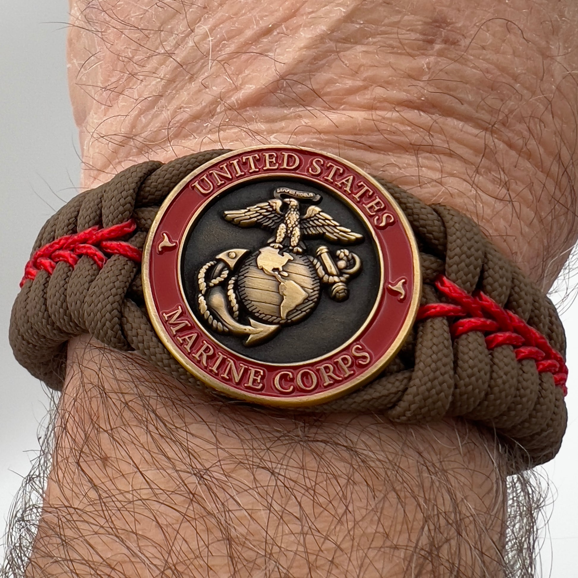 Thick, medium width, semi-rigid and comfortable braided United States Marine Corps bracelet featuring a 24K antique gold plated USMC Eagle Globe and Anchor medallion, a gold Cobra style tactical buckle and woven with Coyote Brown 550 paracord and Imperial Red micro cord.